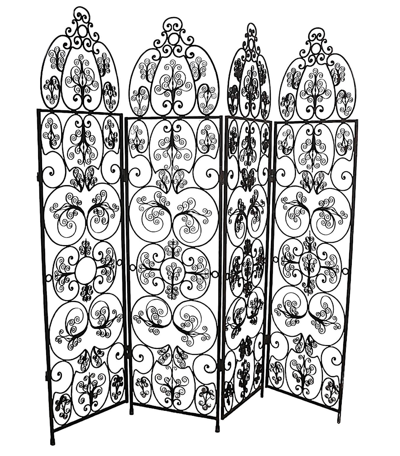Exceptional ornate four fold  wrought iron screen, room divider constructed of four sections each with a cathedral  style top over rectangular panels. 
 The iron is worked into repeating curlicues with an allover pattern. In the style of Woodard,