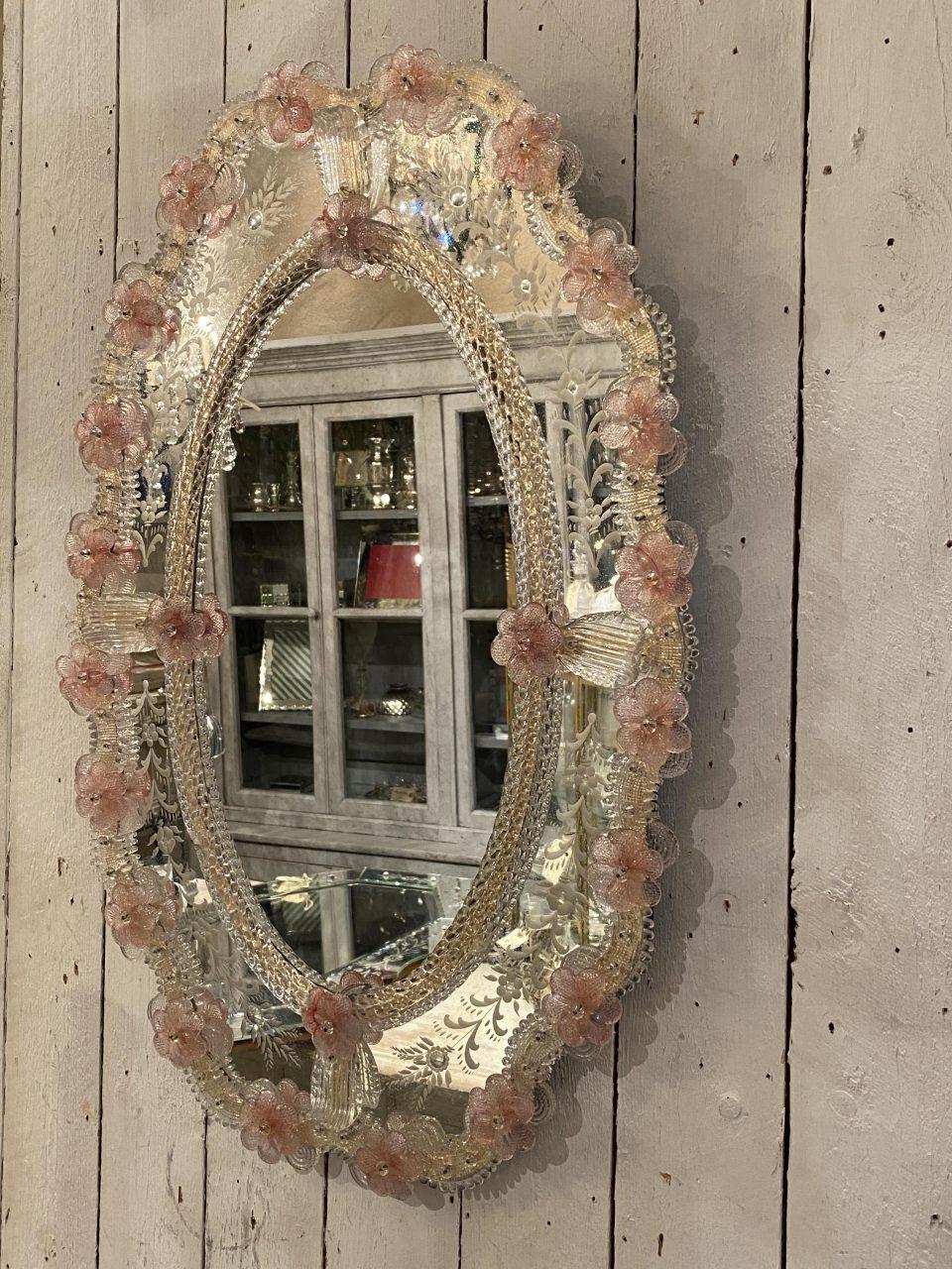 Miroir mural ovale exquis, rêveur, délicat et féminin, de style vénitien, datant des années 1920-40 en France.

Un cadre sophistiqué en verre vénitien et avec d'adorables petits ornements en verre transparent et des fleurs/rosettes en verre rose