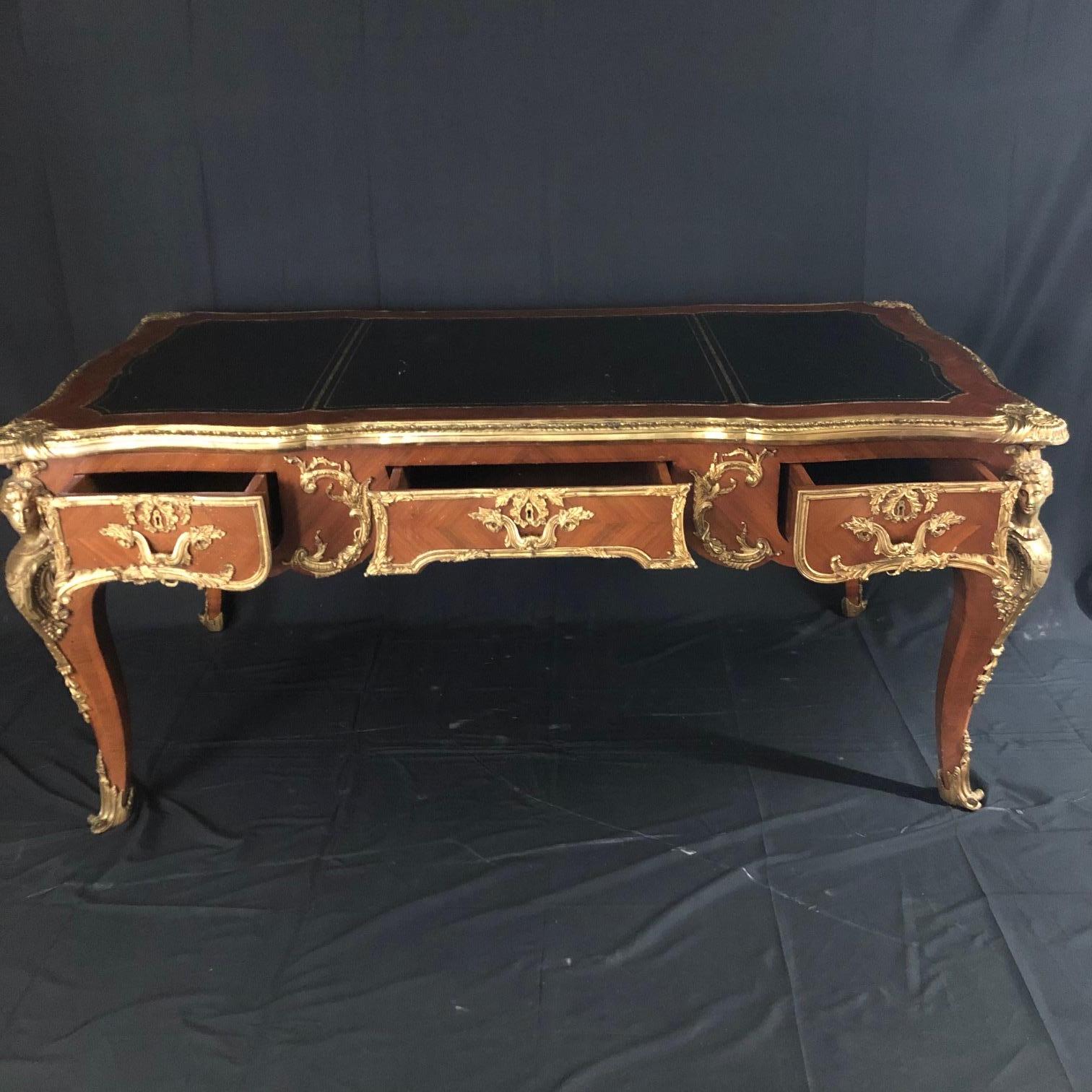 An impressively elegant French Louis XV style walnut and ormolu mounted figural bureau plat desk having herringbone marquetry, rectangular desktop inset with a gilt tooled black leather writing panel, and fitted with three apron drawers with