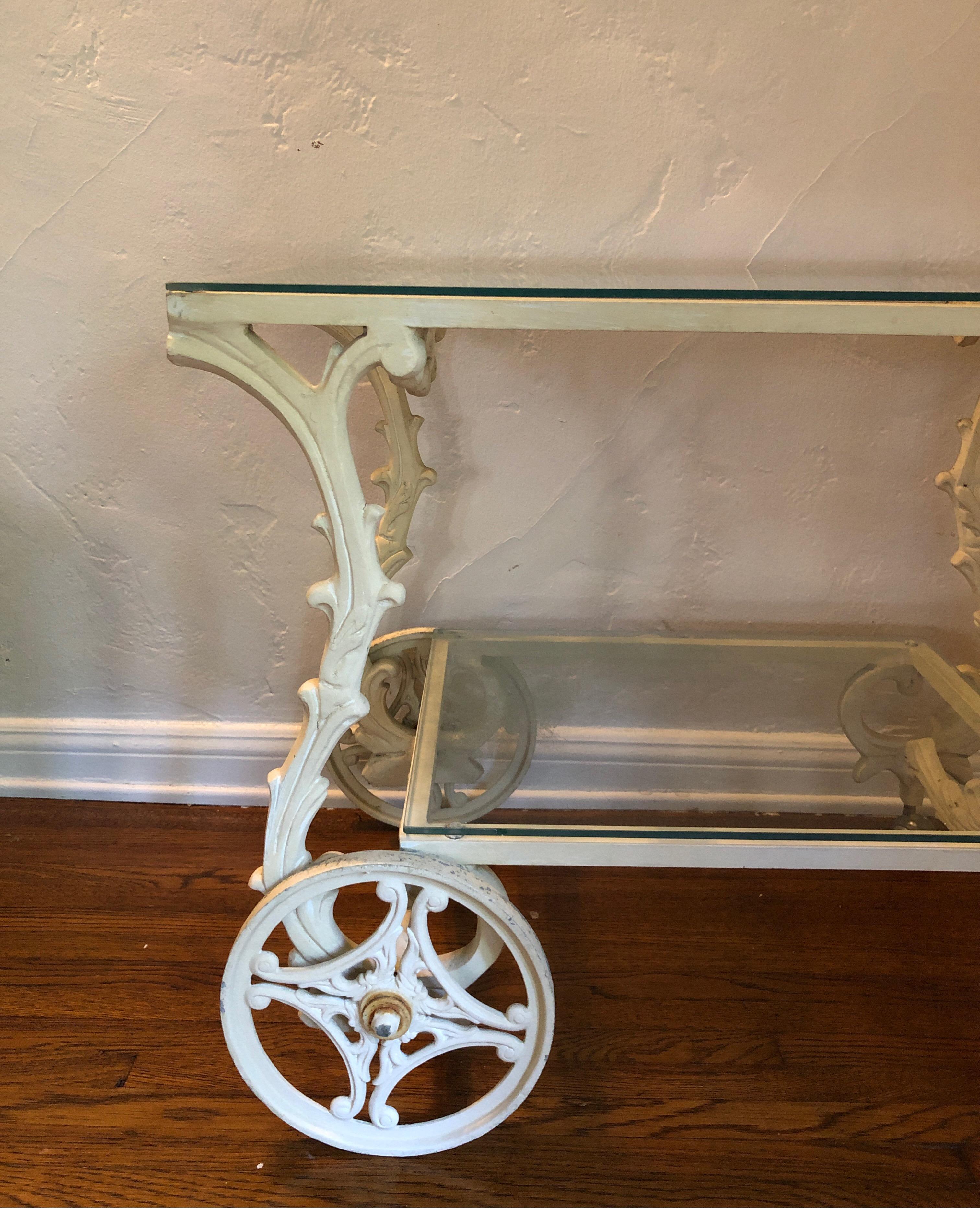 Unique wrought iron bar cart trolley. Perfect for garden server cart. 
Painted ivory/white with interesting curves and details. Two large front iron wheels and two smaller steel wheels. 
Sturdy and rolls but could use restoration if desired. Glass