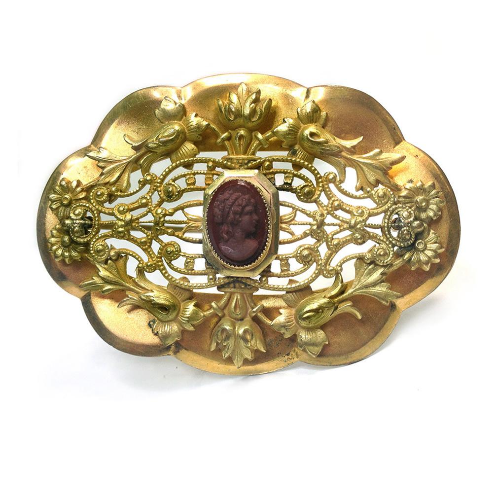 This is a ornate gilt bronze large brooch with a bezel set small burgundy glass victorian style cameo (hair-up female profile) on the top of elaborate open filigree. The 