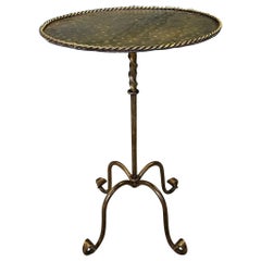 Mesa auxiliar ornamentada de hierro dorado con tablero martillado y patas con volutas