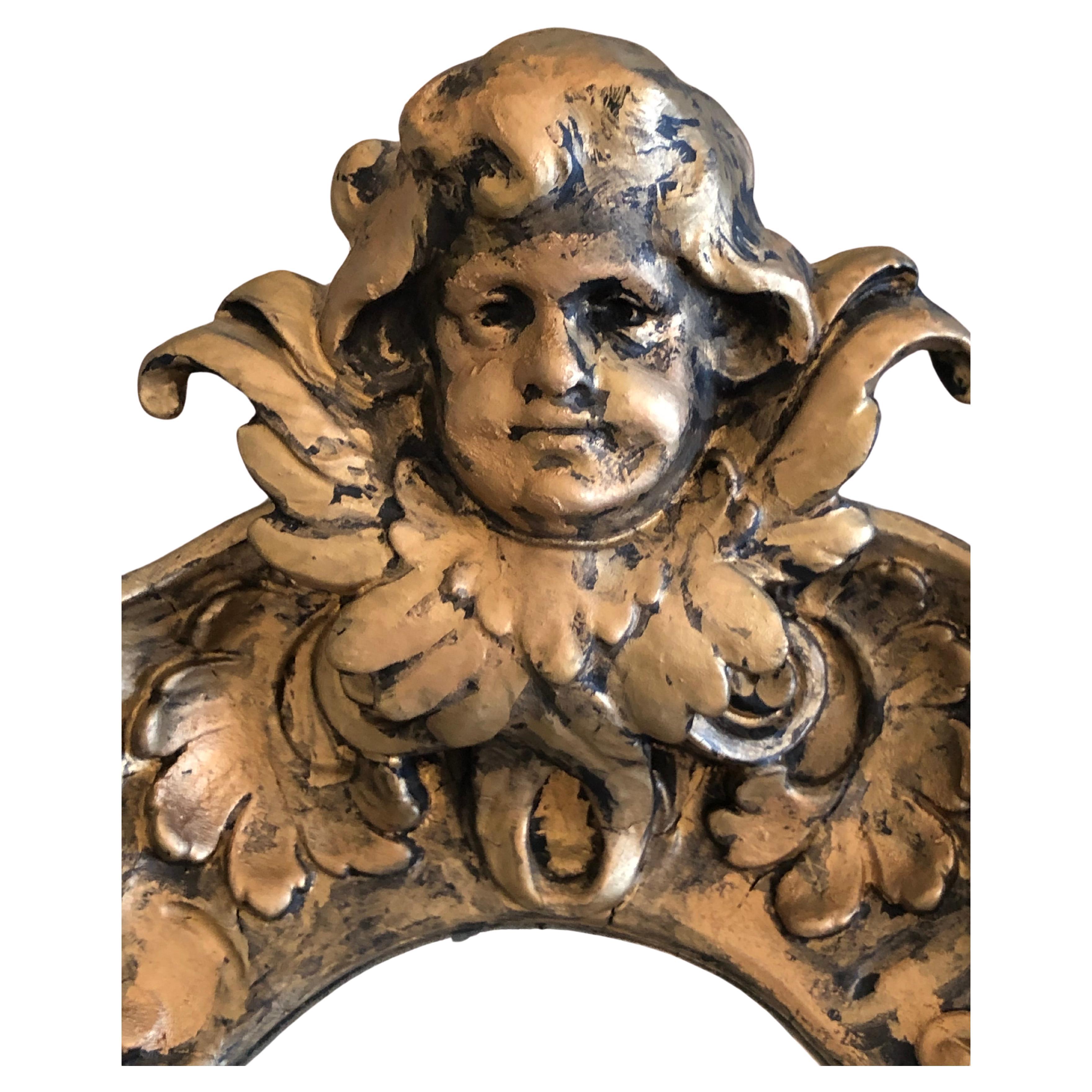 Dramatic Gothic style aged mirror having central cherub at the top, ornate frame and two mask like faces on each side.  Mirror has natural spiderwebs and mercury with fabulous moody patina.