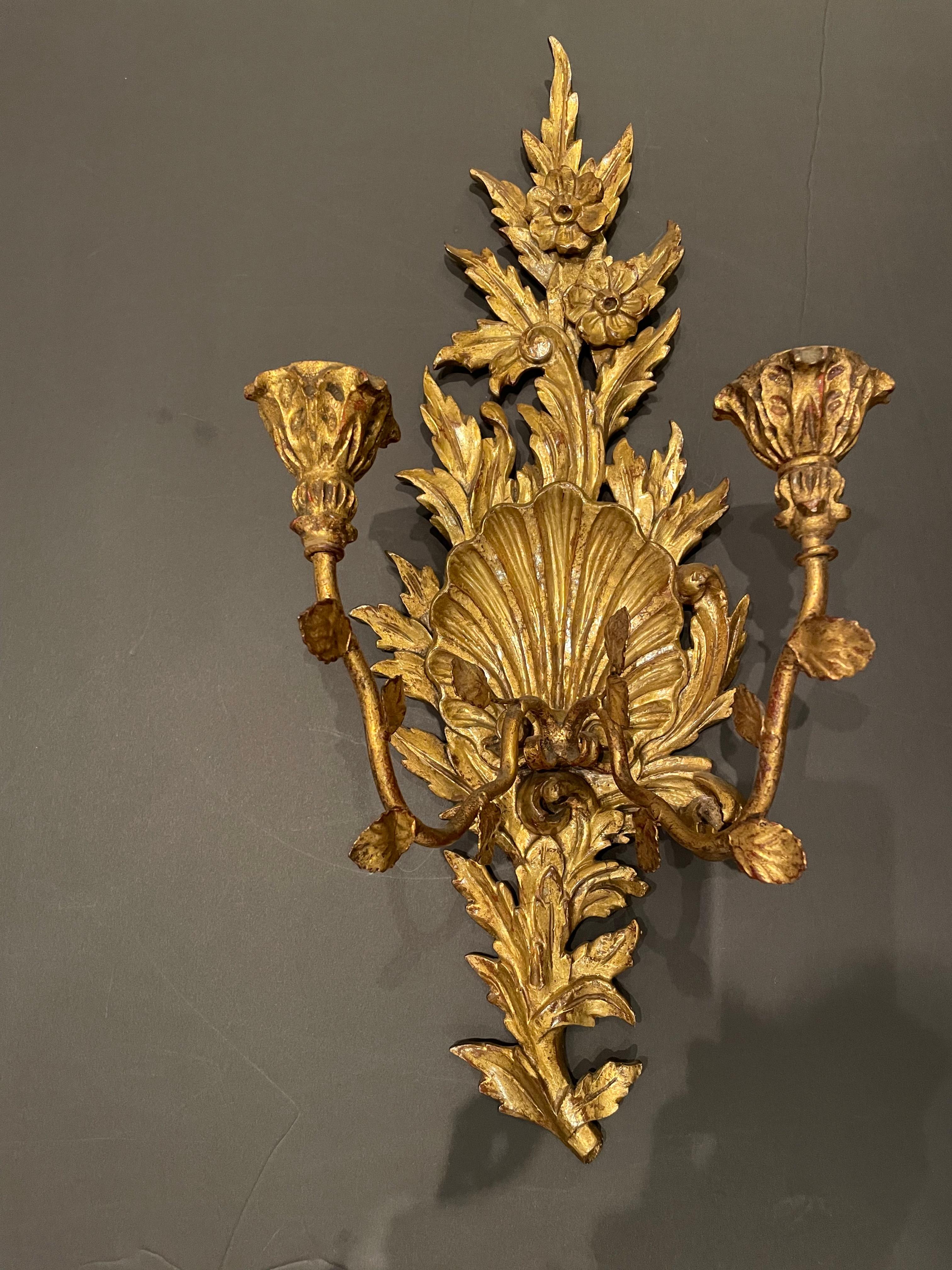 Elegant pair of Italian Rococo style giltwood and metal two arm wall sconces. The center of each sconce has a scallop shell design. The body is constructed of giltwood and the arms are metal in a gilt finish.