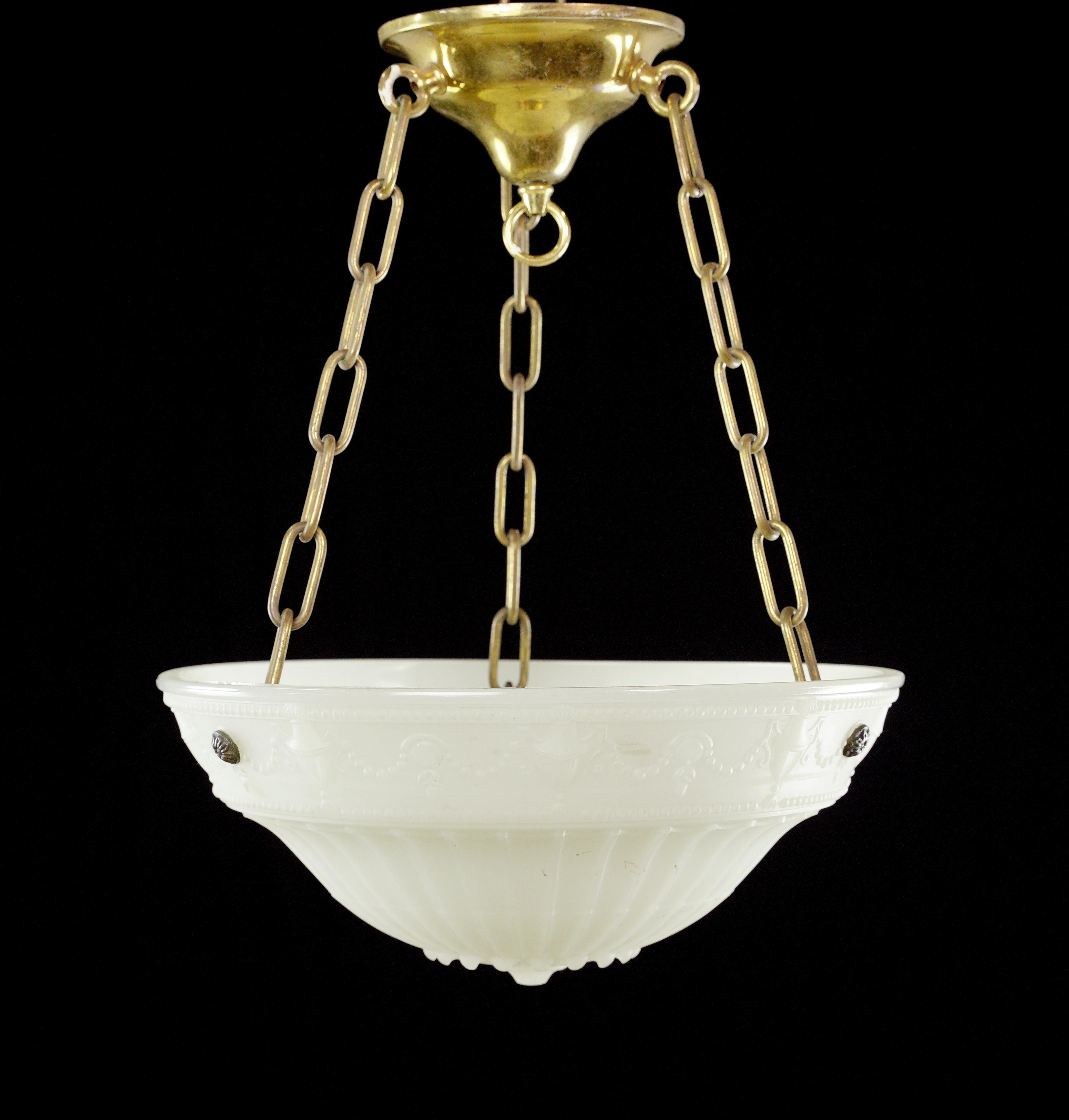 This Victorian pendant light is an exquisite vintage fixture featuring a milk glass dish with intricate ornate designs suspended from a polished brass chain, providing a captivating blend of elegance and nostalgia to any space. This is in good