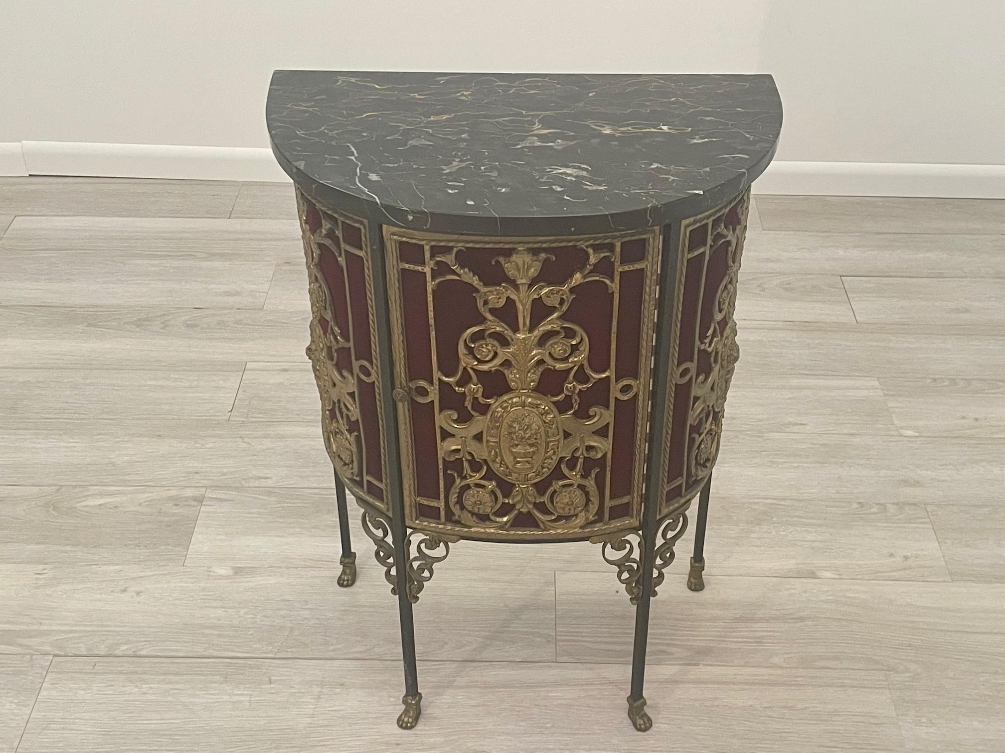 Gorgeous demilune shaped console and cabinet by Oscar Bach having ornate bronze filligree encrusted body with plush red velvet behind the frieze decoration, black marble top and storage inside. Marvelous details including elegant legs that terminate
