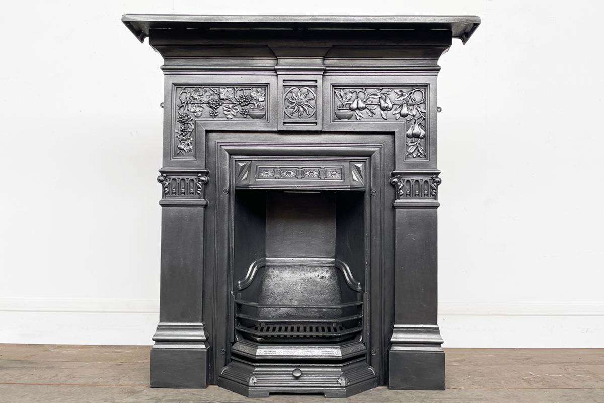 Ornate reclaimed Victorian cast iron combination fireplace. The frieze is decorated with vines and grapes growing from a classical urn on the left and a pear tree bearing fruit growing from another classical urn on the right. The two are separated