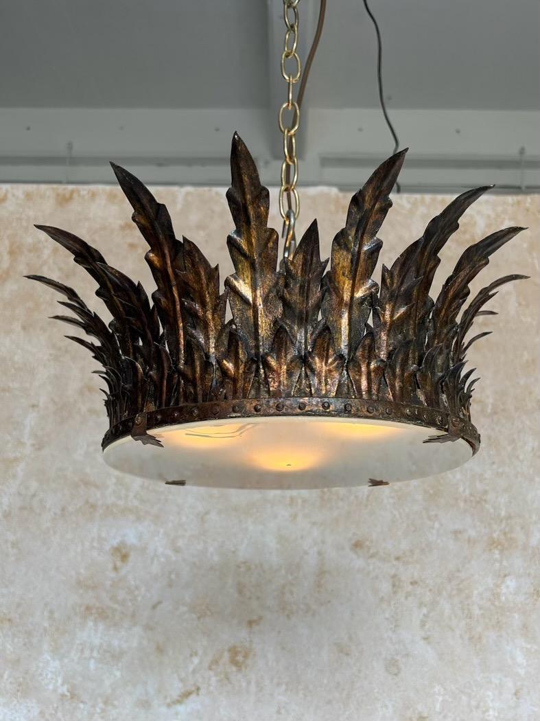 This magnificent Spanish 1950s gilt metal crown ceiling fixture features a sweeping array of alternating long and short leaves surrounding a decorative circular frame that holds the frosted glass center. The beautiful hand applied rich gold patina