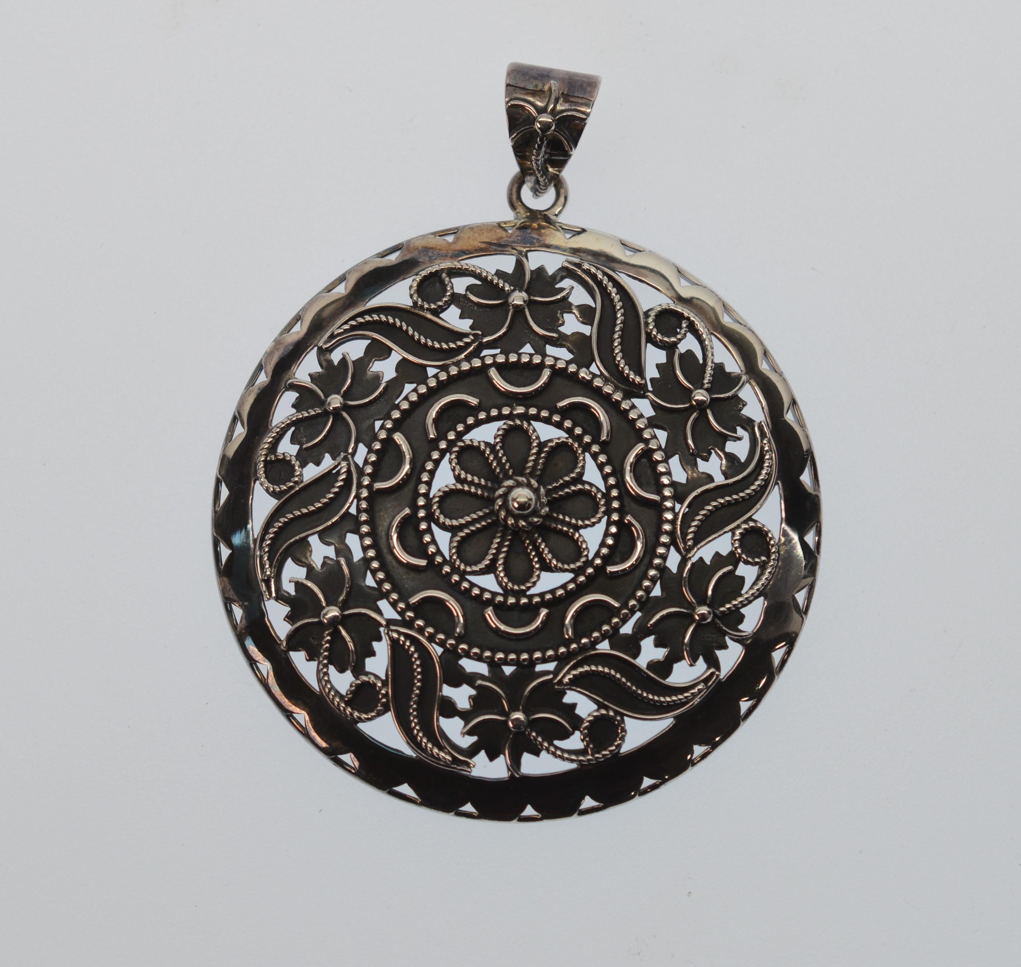 Pendentif en forme de médaillon en argent sterling, avec des volutes appliquées à la main sur de l'argent sterling oxydé pour mettre en valeur les détails et le savoir-faire. Mesure  d'un diamètre de 2-1/4 pouces, le pendentif est équipé d'une anse