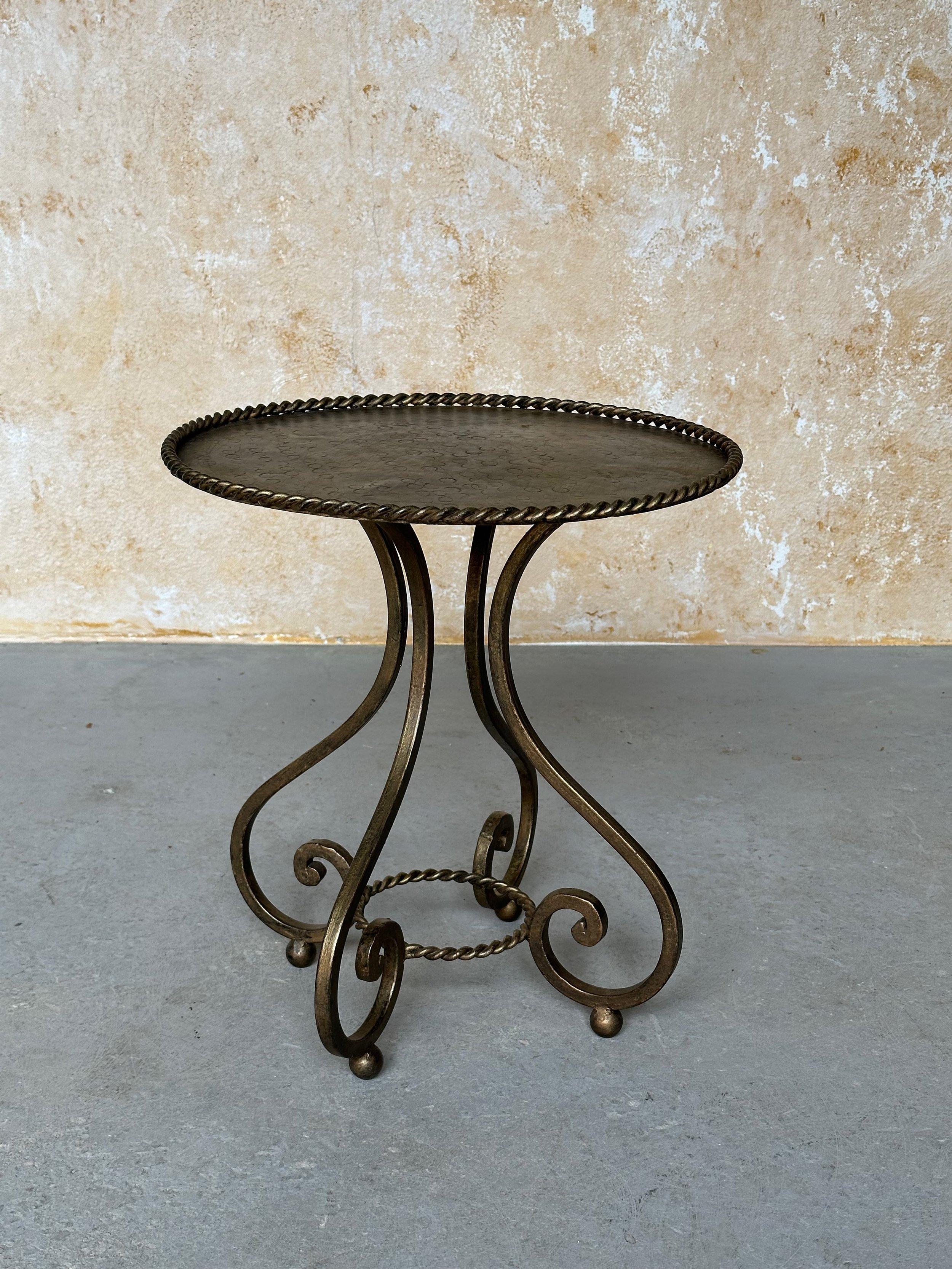 This unique vintage Spanish gilt iron side or drinks table features an ornate intricately shaped hand forged base with four gracefully scrolled legs mounted on ball feet and joined with a central braided ring. The round hammered top is enclosed with
