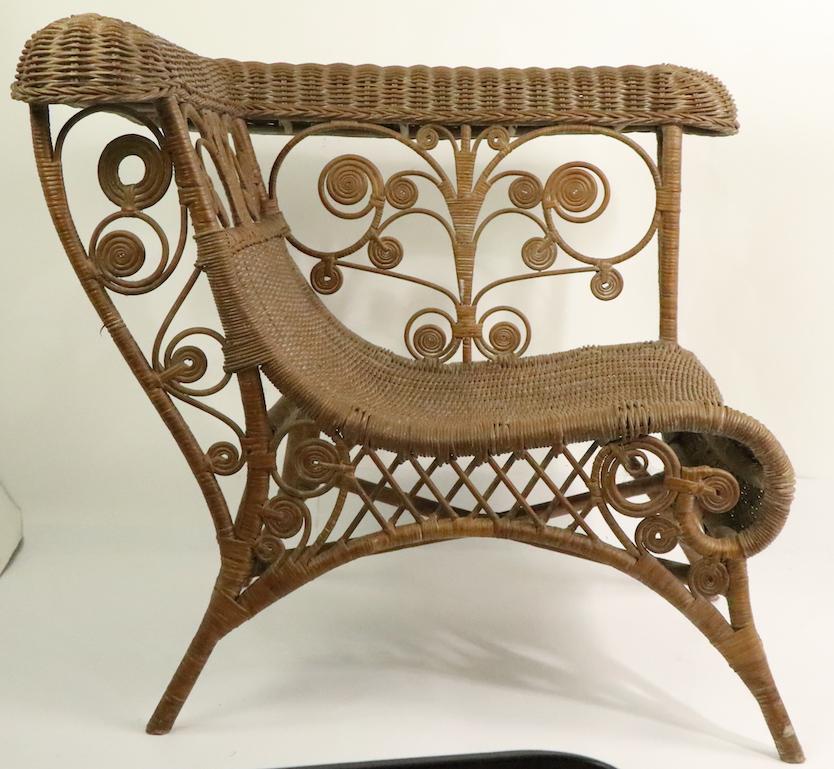 Ornate wicker corner chair in the Victorian style, circa 1970s vintage. Continuous woven wicker seat and back, with rolled woven backrest, and decorative curlicue sides. This example is in excellent, original condition, free of breaks, loss, or