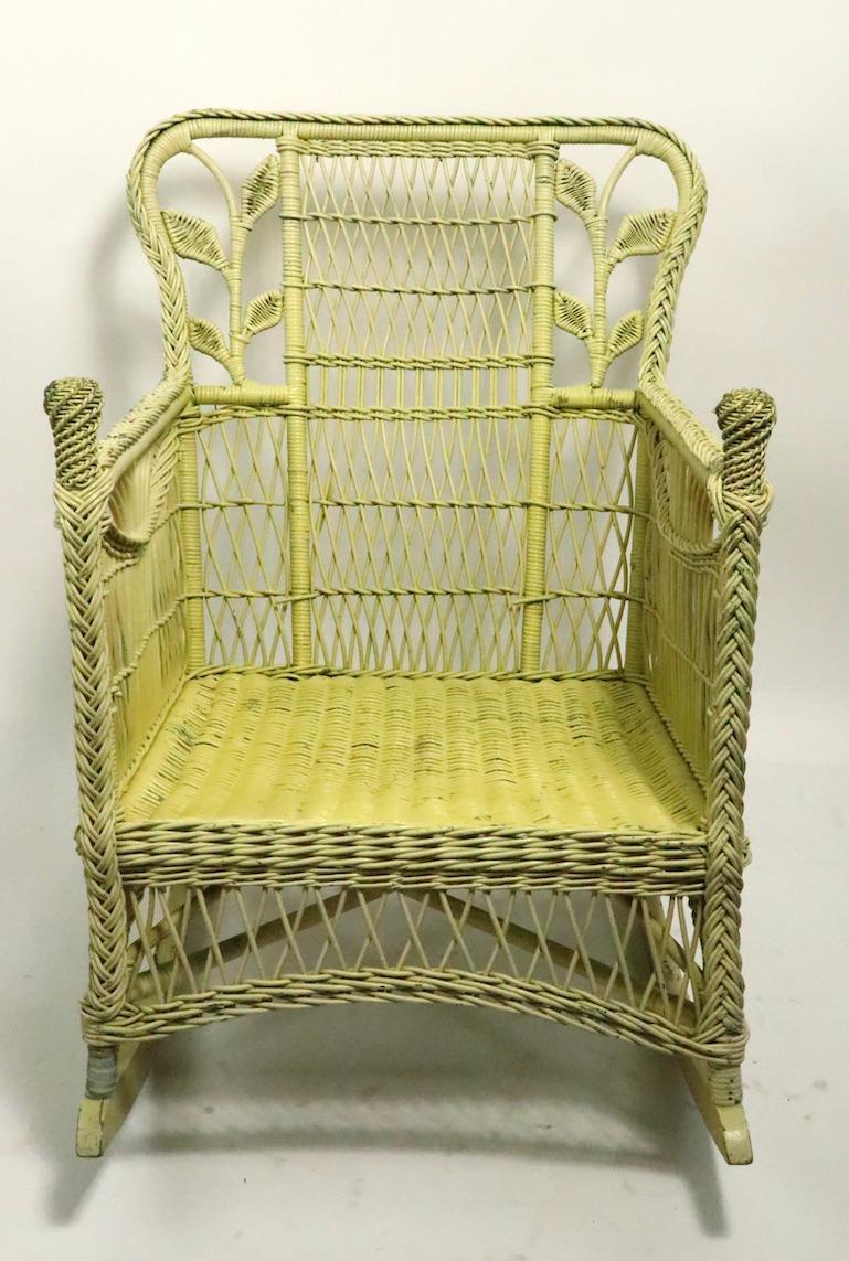 Ornate wicker rocker having decorative woven leaves on the backrest. The chair is in very good condition, solid, sturdy and ready to use, it shows minor cosmetic wear, scuffs etc. normal and consistent with age. The chair is currently in later