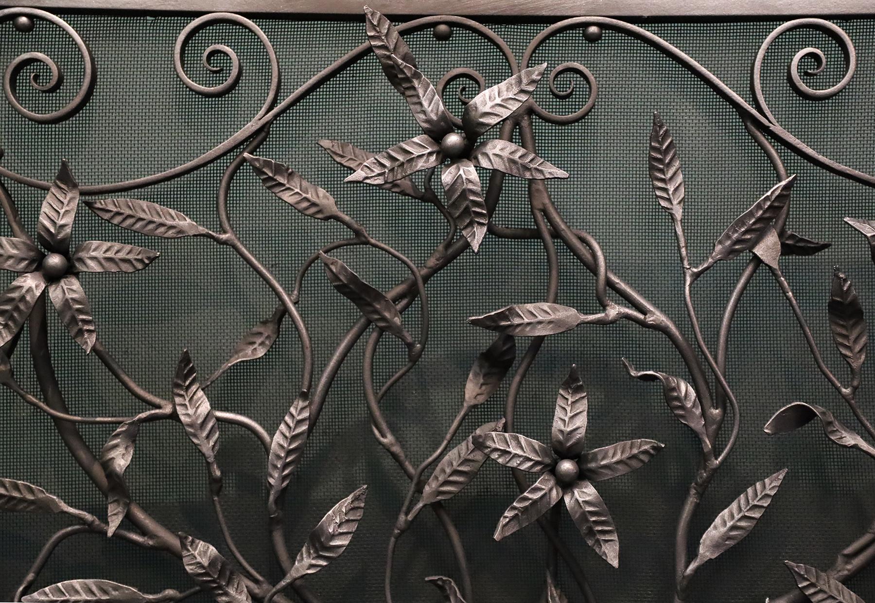 Écran de cheminée en bois ouvragé, orné de volutes et de fleurs sauvages. Le vase central nervuré abrite le feuillage soigneusement arrangé et les fleurs sauvages aux formes exquises, encadrées par des volutes, le tout sur des supports arqués.