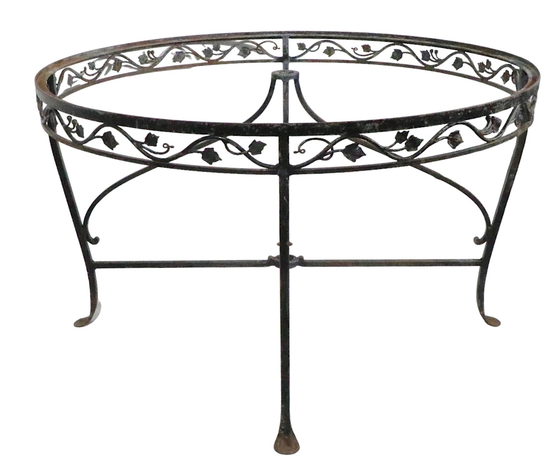 Exceptional wrought iron dining table having an ornate foliate motif skirt, curved legs and paw feet. The table is designed to accept a sun umbrella in the center, having a support directly under the glass top and a second support at the