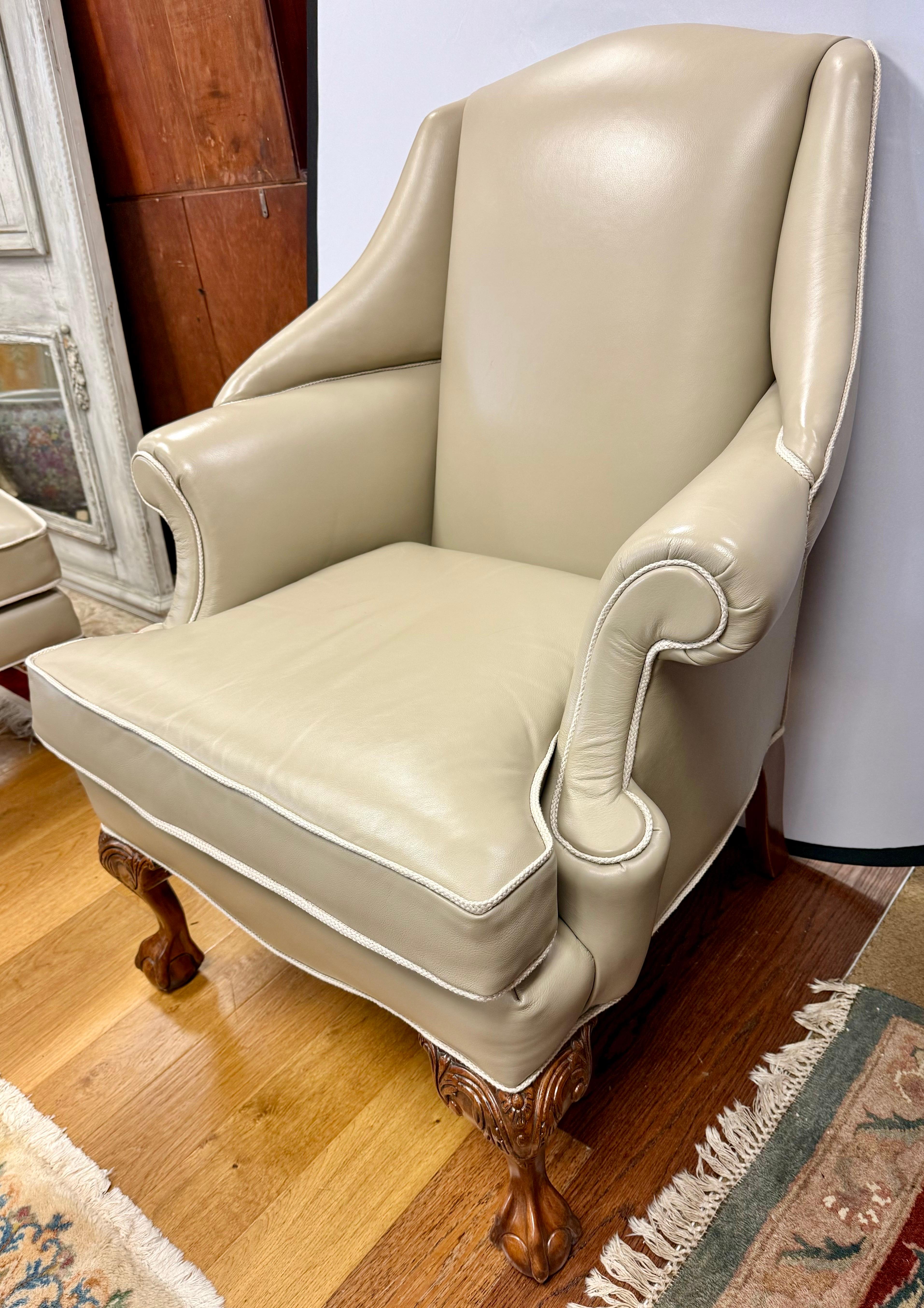 Vintage chippendale style oversized wingback library club chair and matching ottoman combo.  Features neutral taupe leather upholstery with contrasting piping and carved mahogany frame.  Both pieces are supported by carved ball and claw feet which