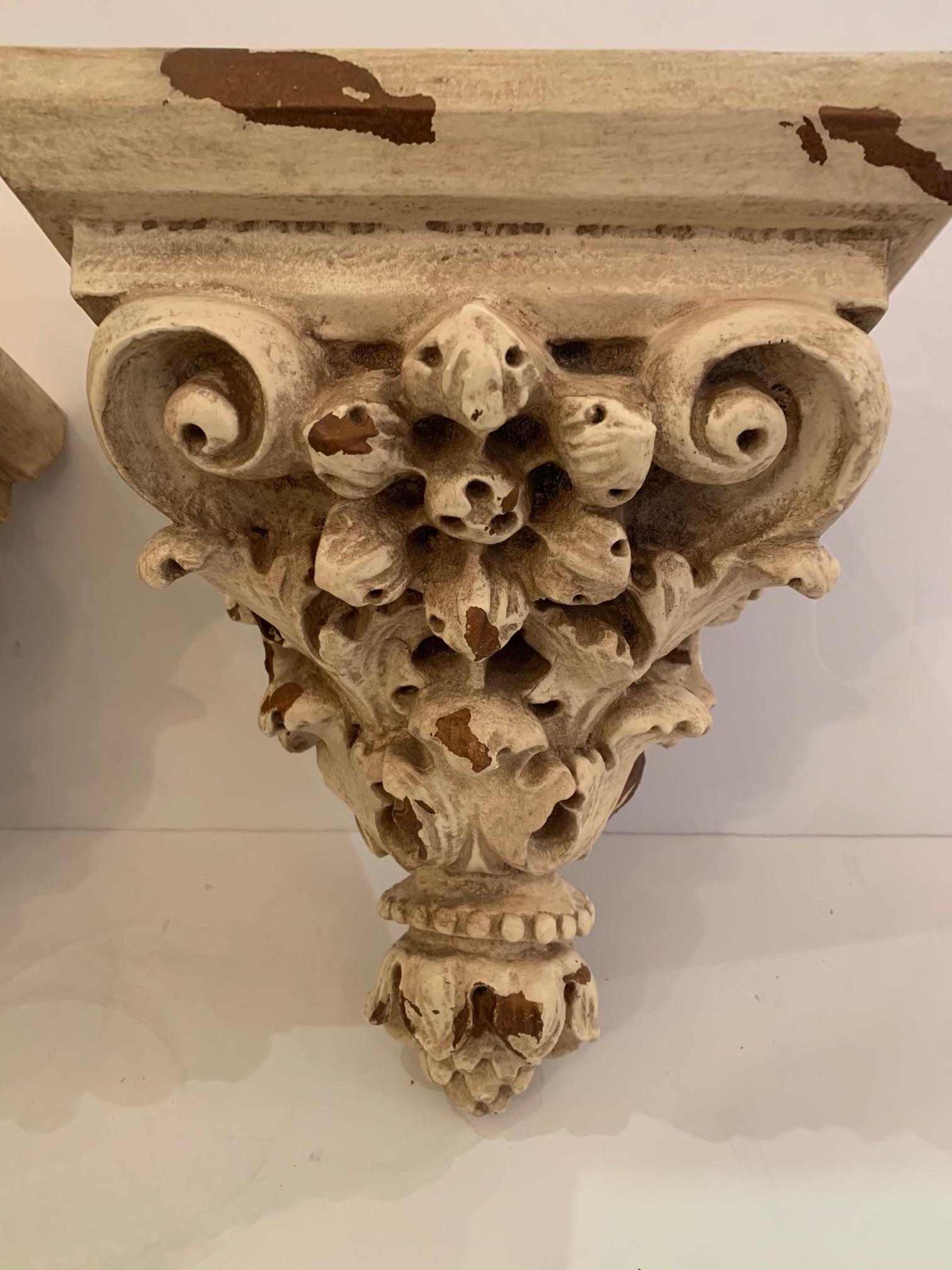 Elegant pair of ornately carved wall brackets having a chippy off-white and natural patina.
Mark on back reads Design Source, 1999.