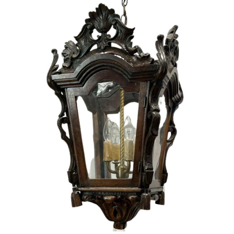 A rococo style four sided wood lantern with four lights. Each glass panel is topped with arched wood and surrounded with ornately carved detail as well as raised, carved foliate details to the sides of each panel. Bottom of each corner features a