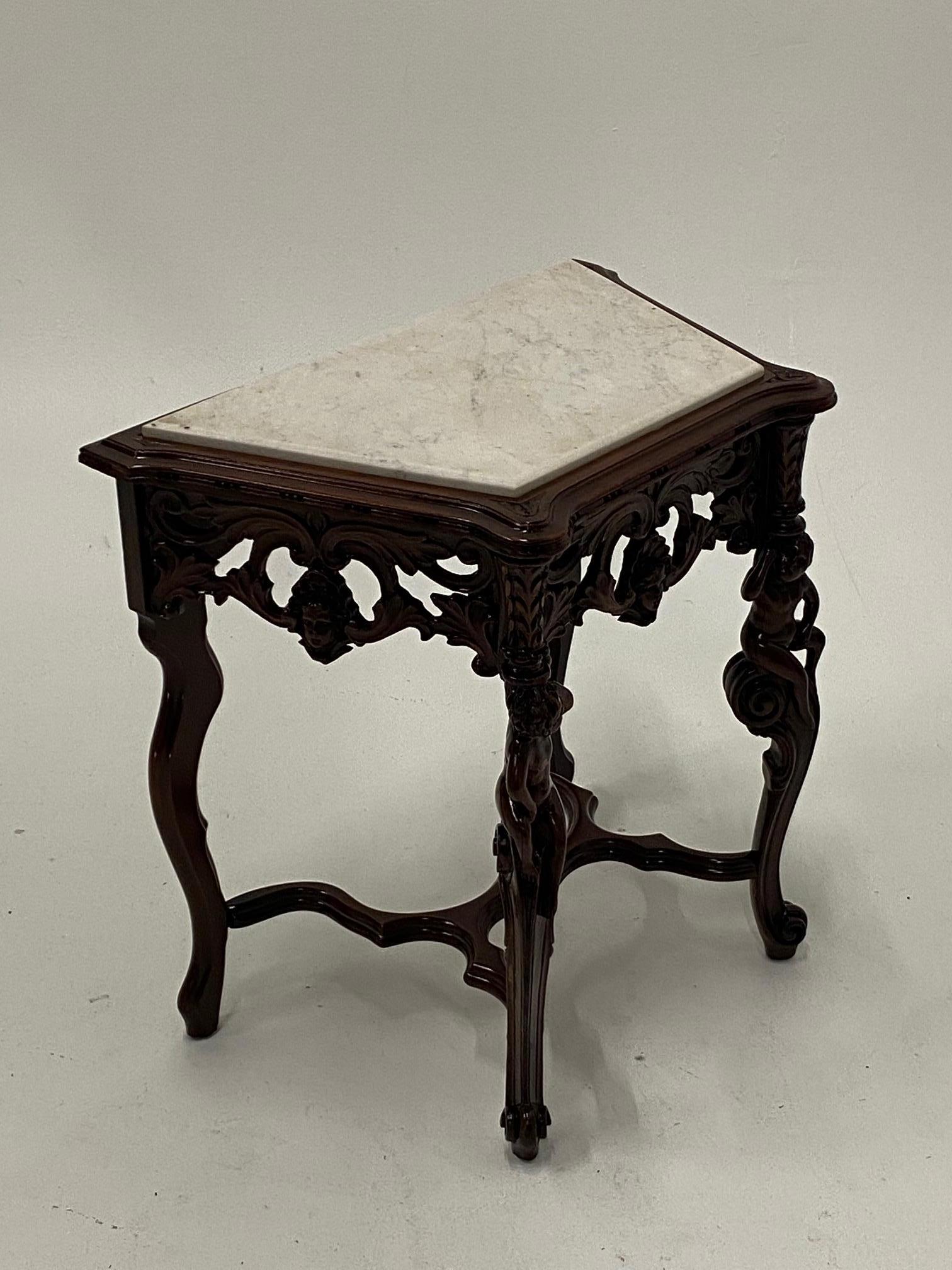 A lovely vintage side or end table with an interesting skewed rectangular shape and ornately carved mahogany base with putti. Top is original white marble.