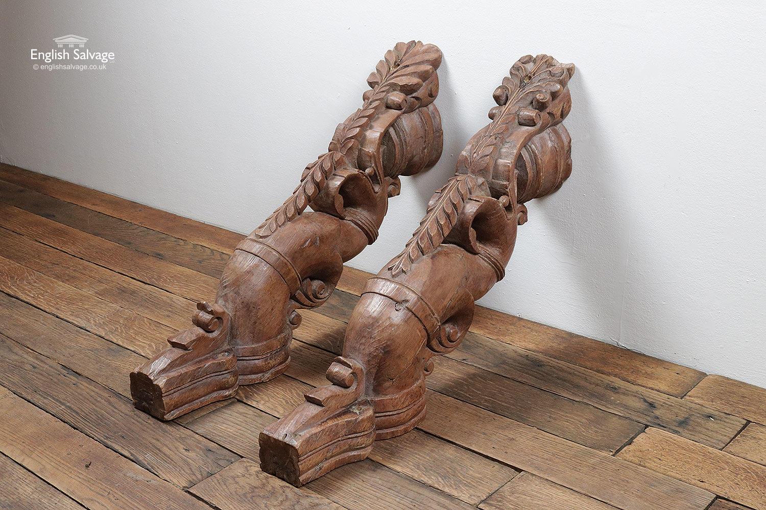 A pair of reclaimed, hardwood corbels. These are rustically hand carved in teak in an Indian style. Chisel marks, small cracks and imperfections add to their rustic charm. Features of the carving include a vertical leaf garland with a small ball to