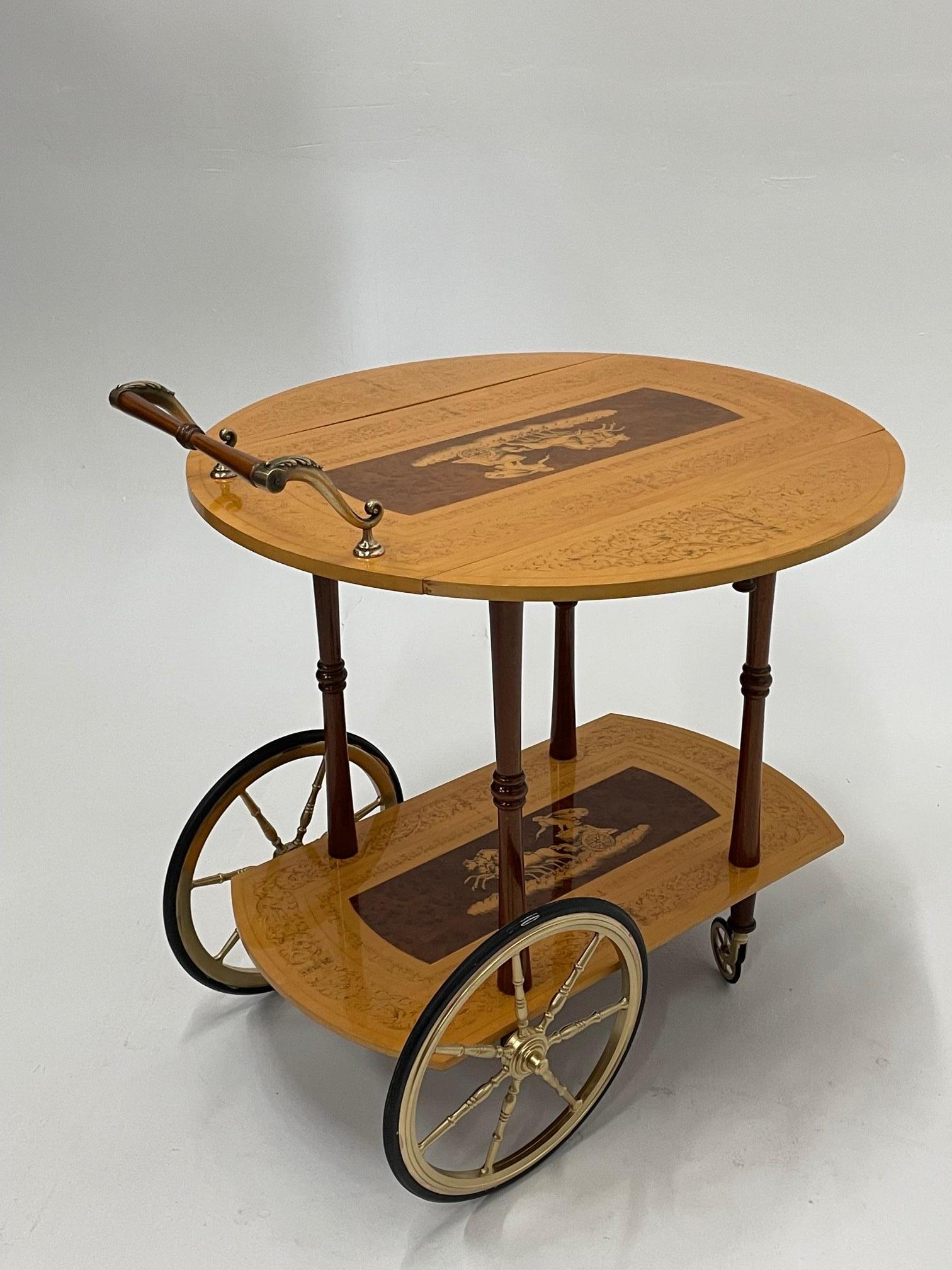 A lovely birch and mahogany bar cart having stencil decoration and inlaid chariot scene with drop leaves, bottom tier, and gorgeous brass wheels and handle. When leaves are extended the cart is round and 27.5 diameter. 16.5 D with sides down
Artist