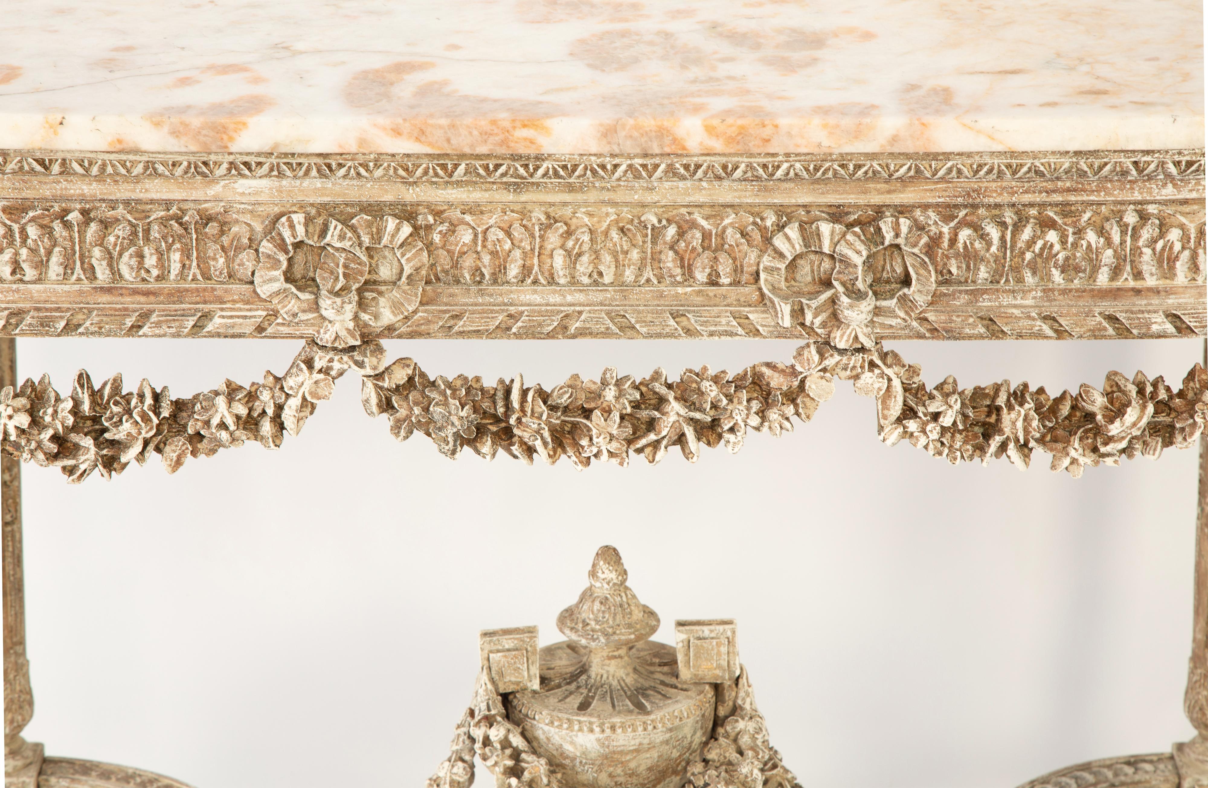 Louis XVI center table or console, finished on all sides, having a rectangular top of breccia marble with slightly-bowed front and rear edges. Its elaborately hand-carved table base with a distressed, painted finish, and gadrooned apron over a