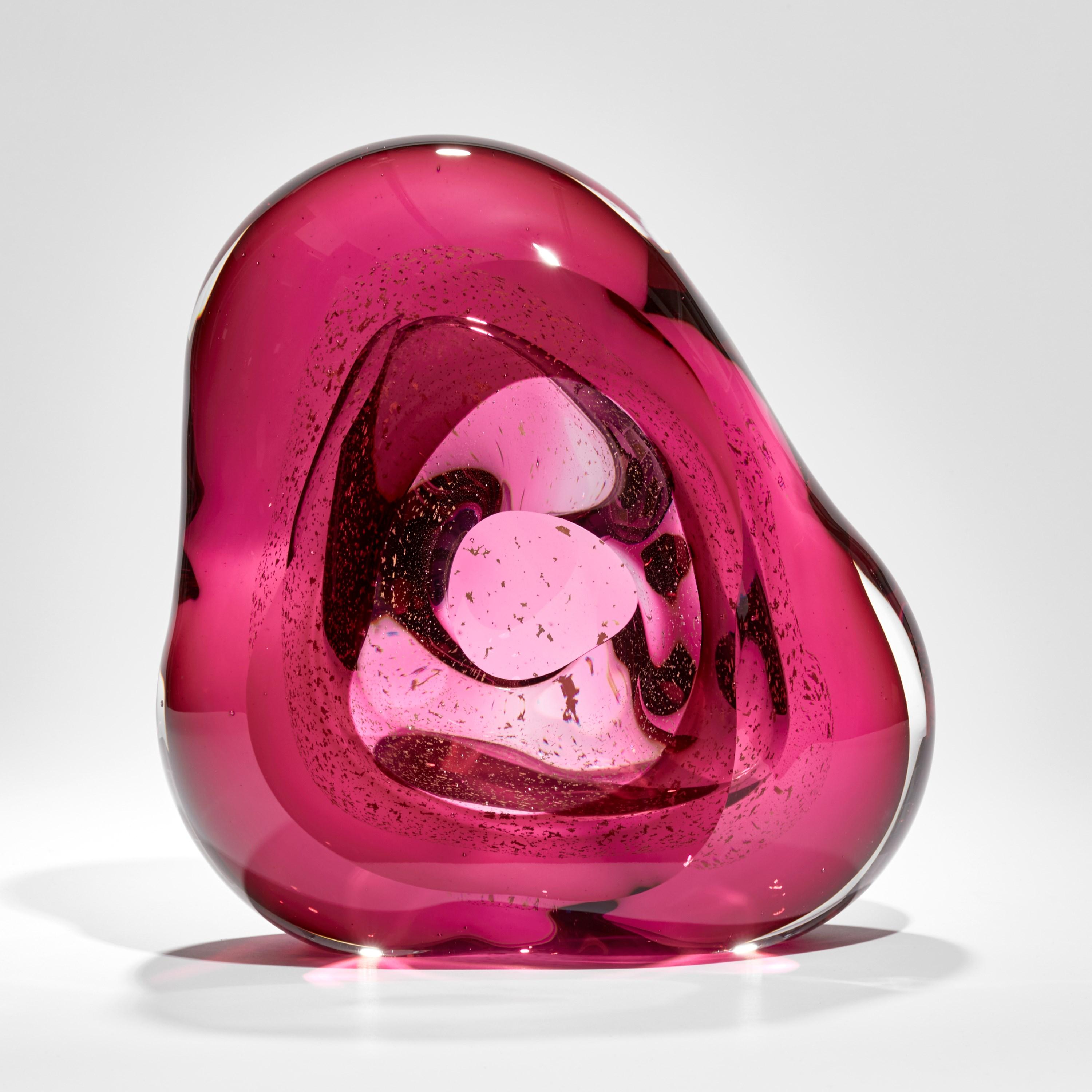 'Oro Vug in Fuchsia I' is a unique handblown pink glass sculpture by the British artist, Samantha Donaldson. Created from layers of clear and rich fuchsia pink coloured glass with 24 carat gold leaf, these elements merge creating the illusion of