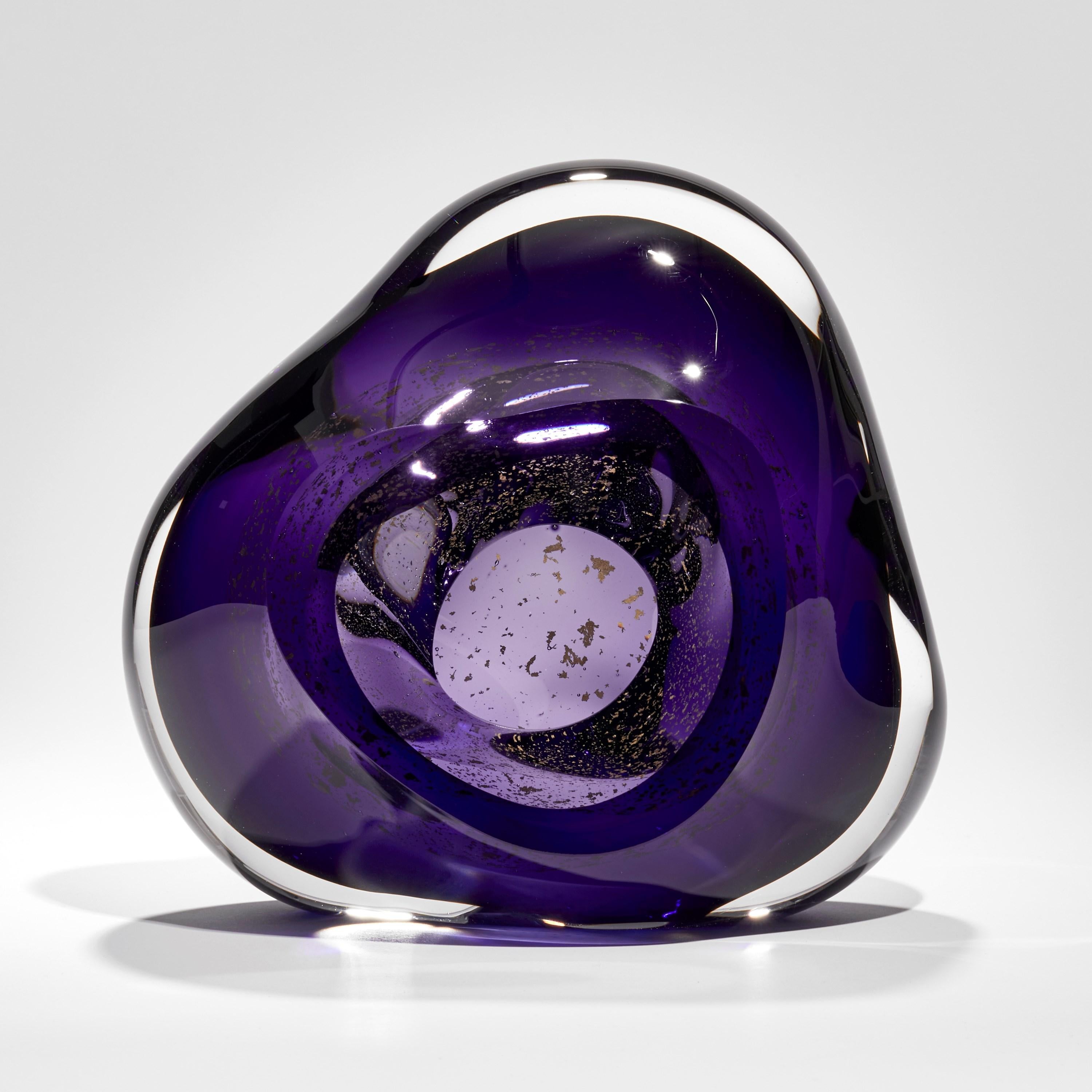 'Oro Vug in Purple I' is a unique handblown glass sculpture by the British artist, Samantha Donaldson. Created from layers of clear and rich purple coloured glass with 24 carat gold leaf, these elements merge creating the illusion of swirling gold