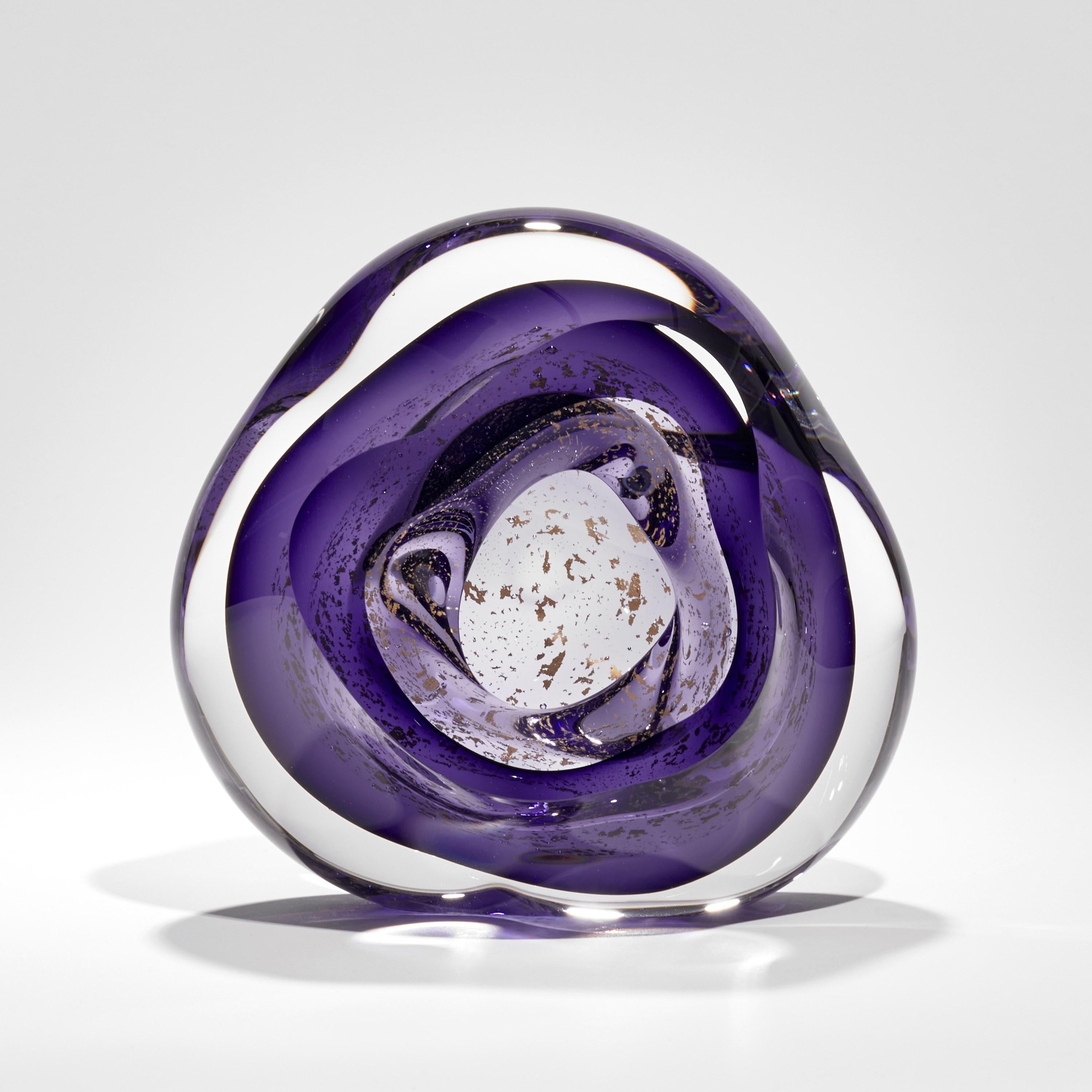 'Oro Vug in Purple II' is a unique handblown glass sculpture by the British artist, Samantha Donaldson. Created from layers of clear and rich purple coloured glass with 24 carat gold leaf, these elements merge creating the illusion of swirling gold