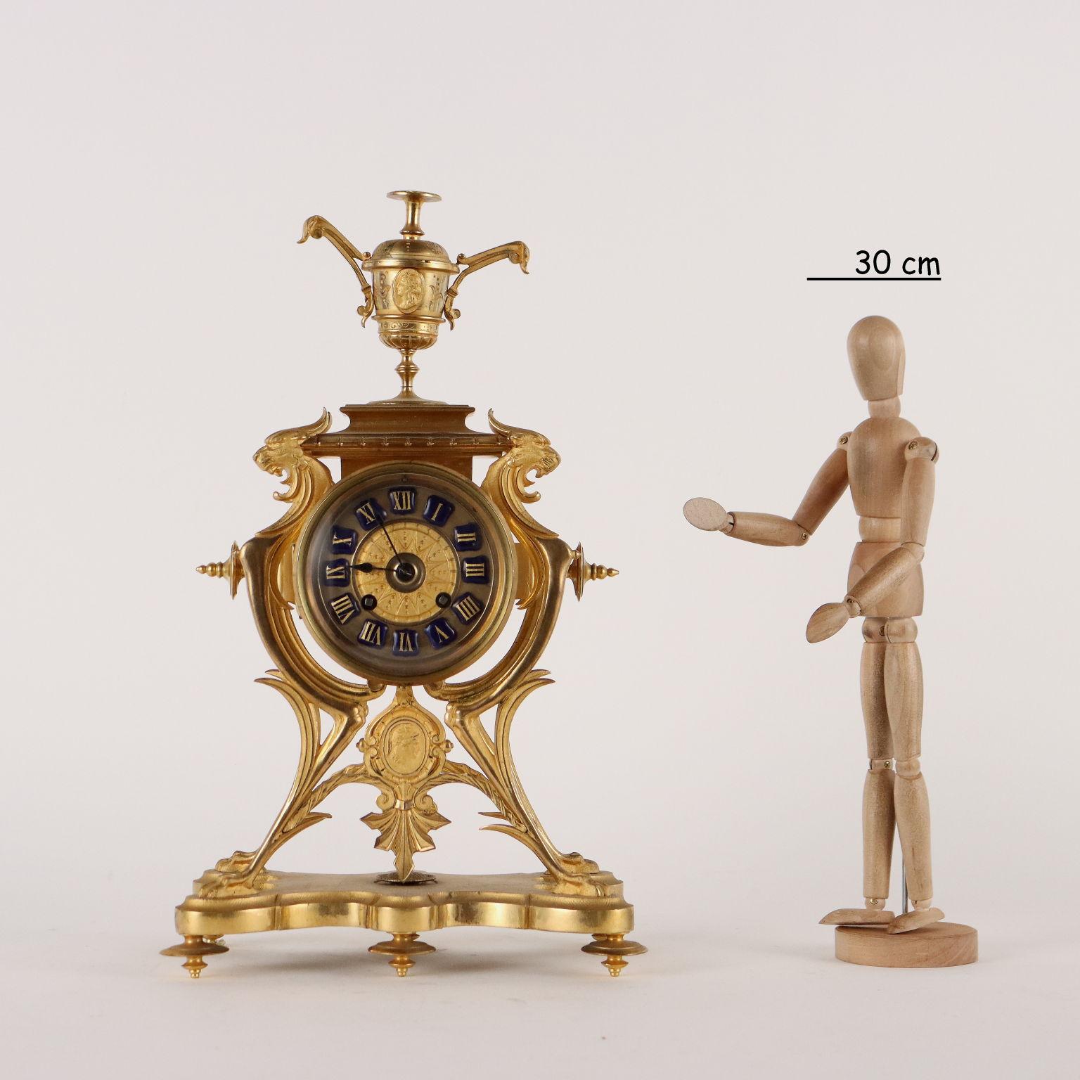 Gilt bronze standing clock. The clock with bronze display and Roman numeral hours in blue enameled metal is held by four fantastic animals resting on shaped base. Under the clock medallion with soldier's head and at the top vase with cameos. Gilt