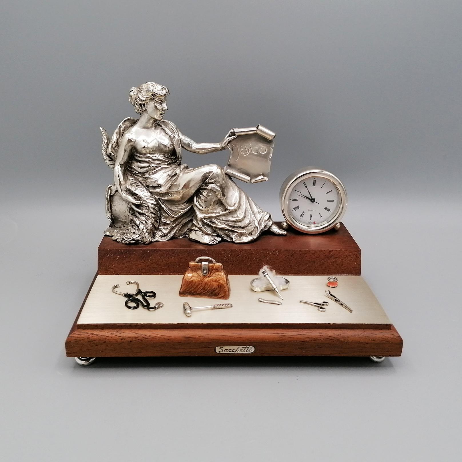 Miniature and Sterling Silver Desk Clock  and wood. 
The base is made of wood. Above it, the following 925 silver parts were made and placed:
Goddess of Fortune holding a scroll engraved 