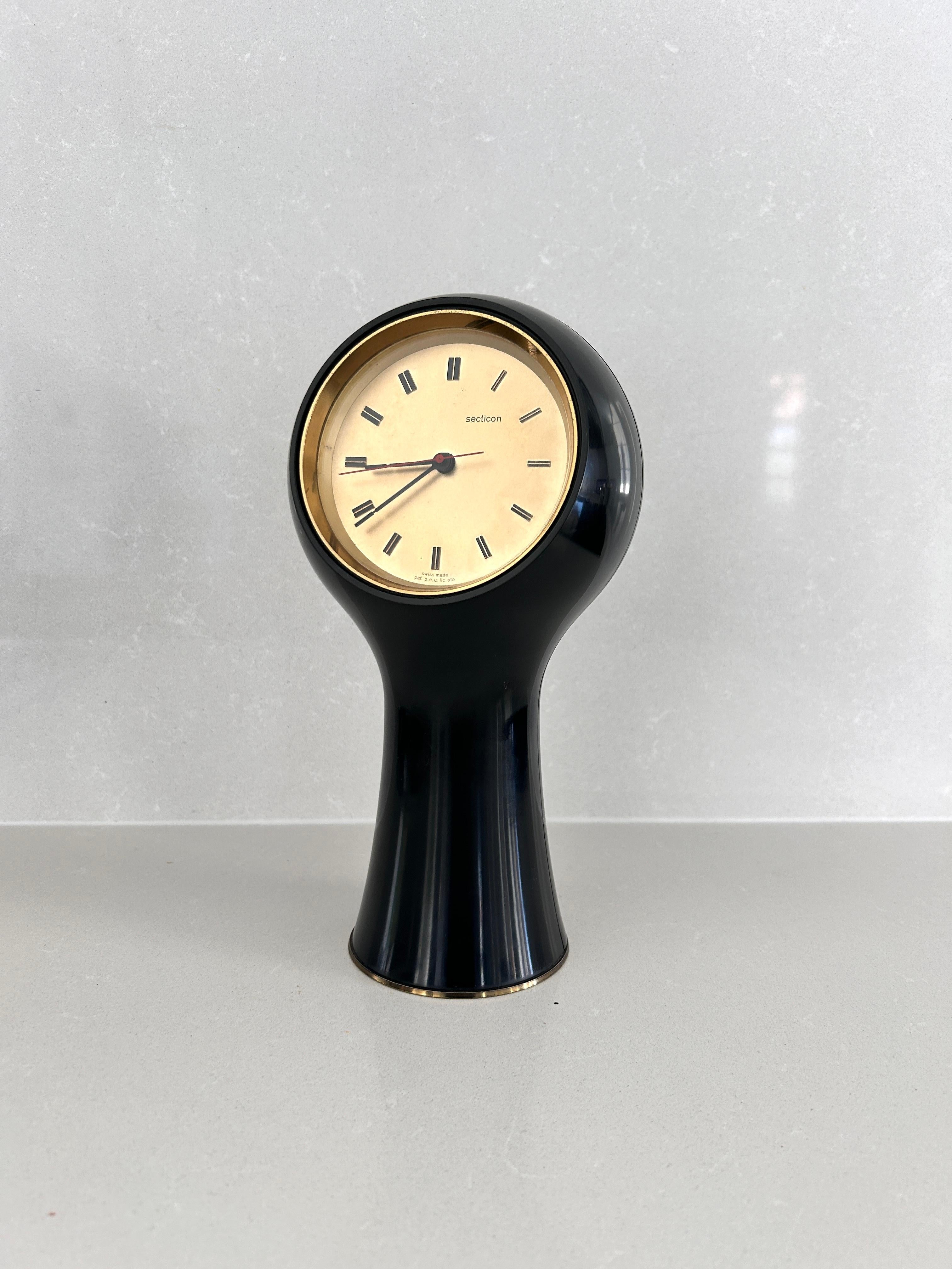 Tischuhr, entworfen von Angelo Mangiarotti und Bruno Morassutti im Jahr 1956 für die Schweizer Firma Le Porte-Echappement Universel.  

Schwarzer Kunststoffrahmen, batteriebetriebenes Uhrwerk.