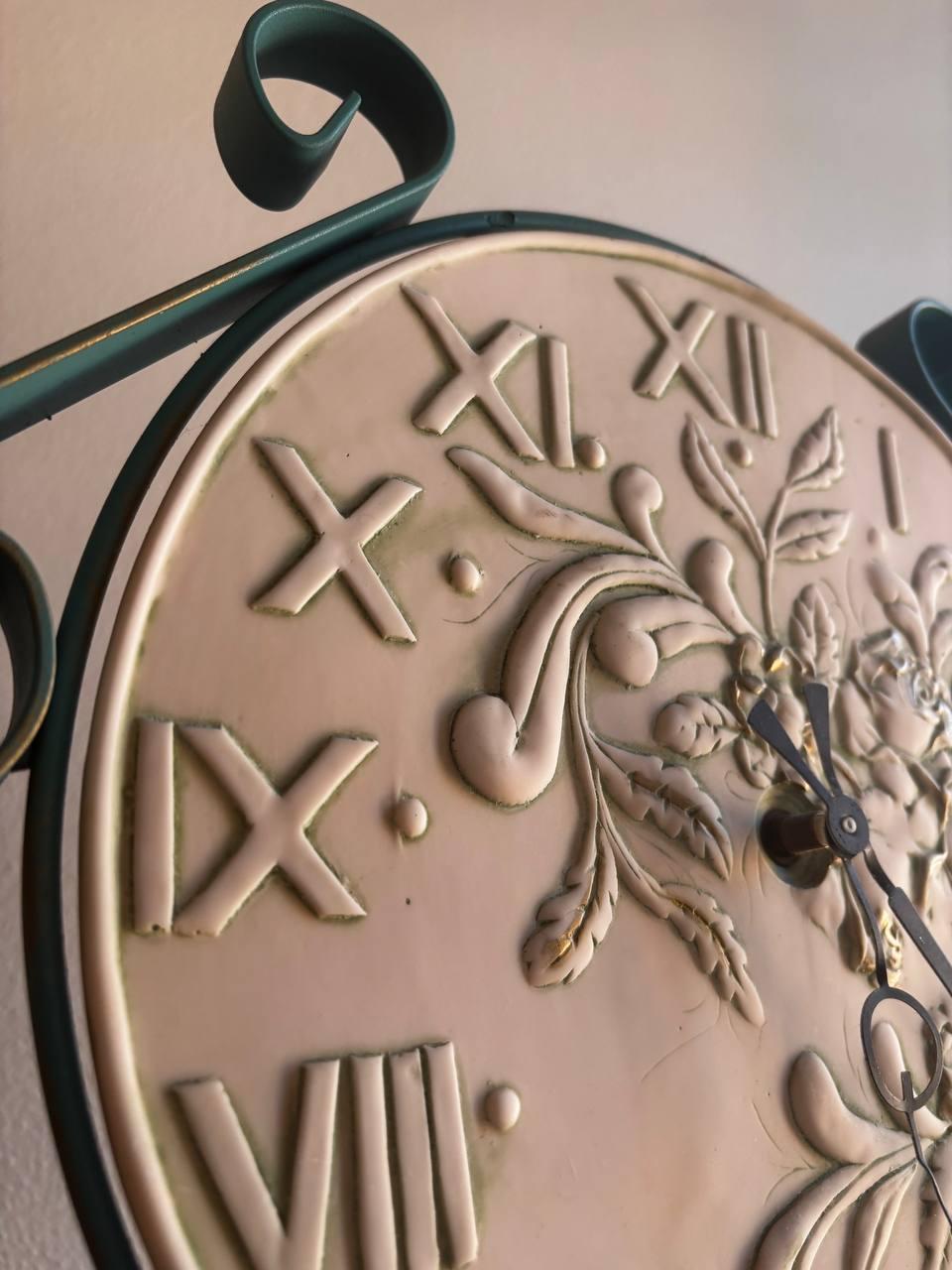 The object shown in the image is a stand or column clock. This type of clock is designed to be placed on the floor, serving as a piece of furniture. The model shown has a metal frame, probably wrought iron, with a circular base and a rod supporting