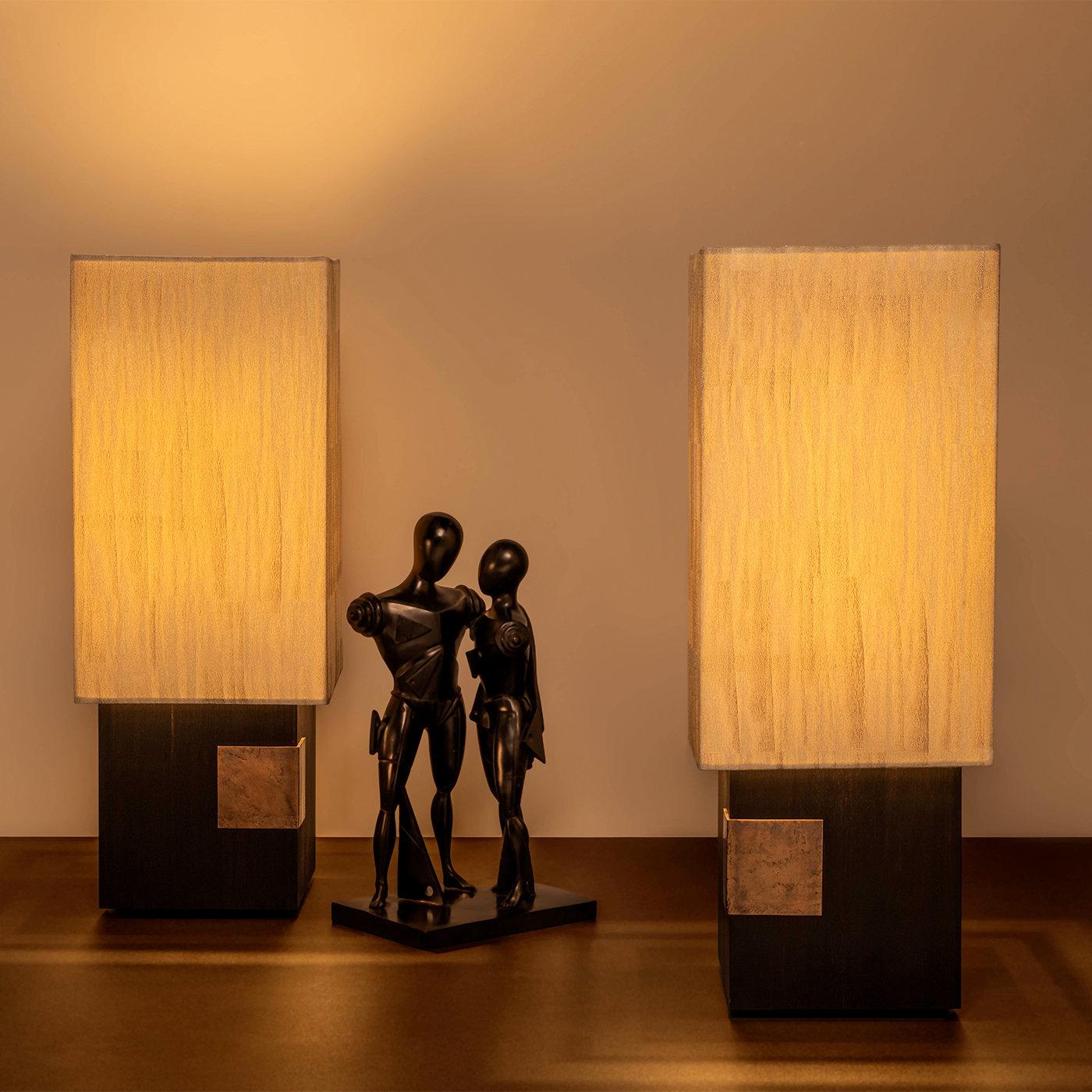 Table lamp with base in top-quality African ebony wood. The bronze detail functions as a touch switch by means of a sensor that dims the led circuit. The decorative jacquard fabric is inspired by hand-made drawing recalling the art deco style. The