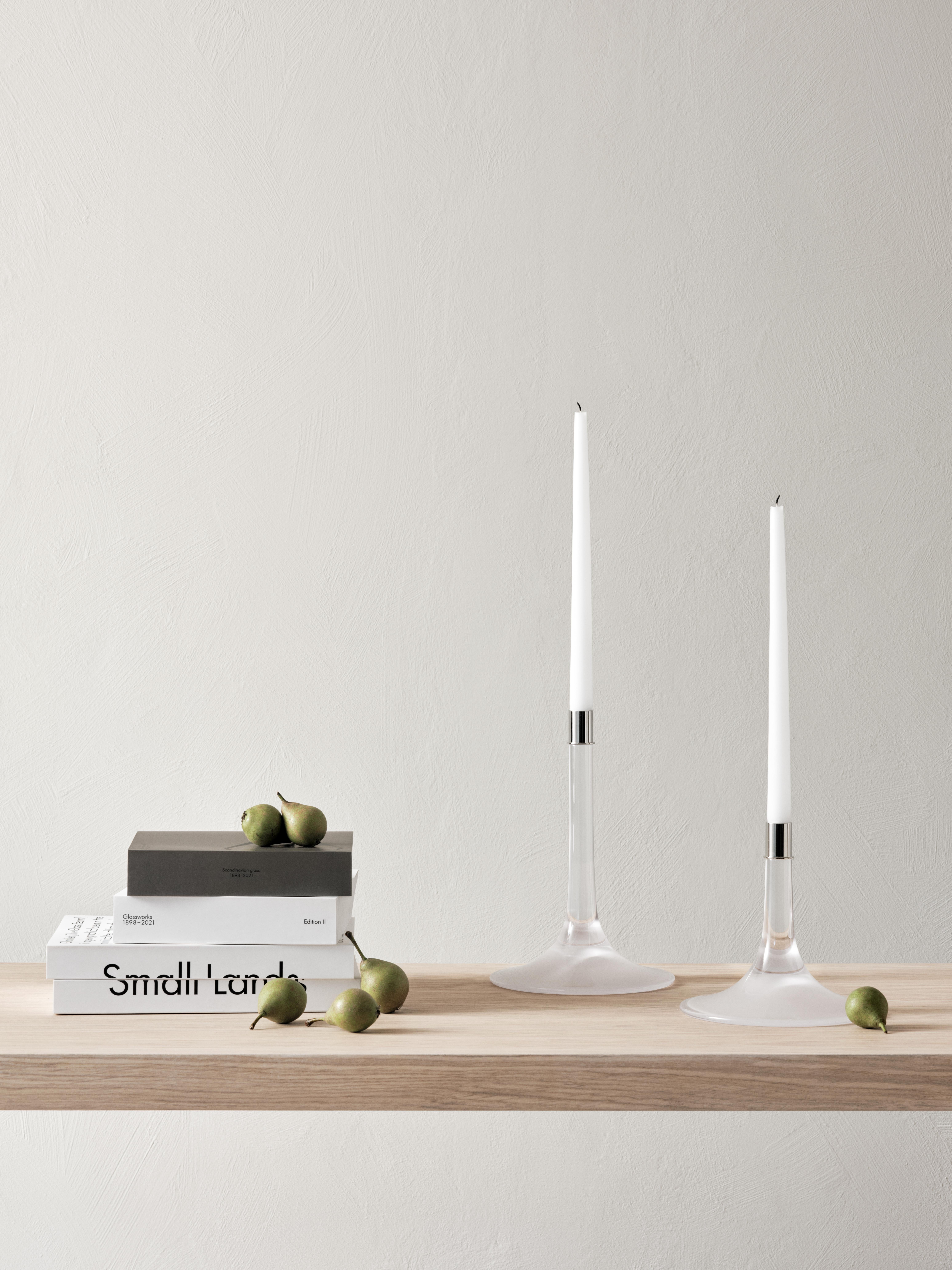 Cirrus Candlestick Medium from Orrefors is a candlestick with a large base, a distinctive feature contributing to its identity. The base with a sandblasted underside provides a soft transition to the clear crystal rod, which refracts and beautifully