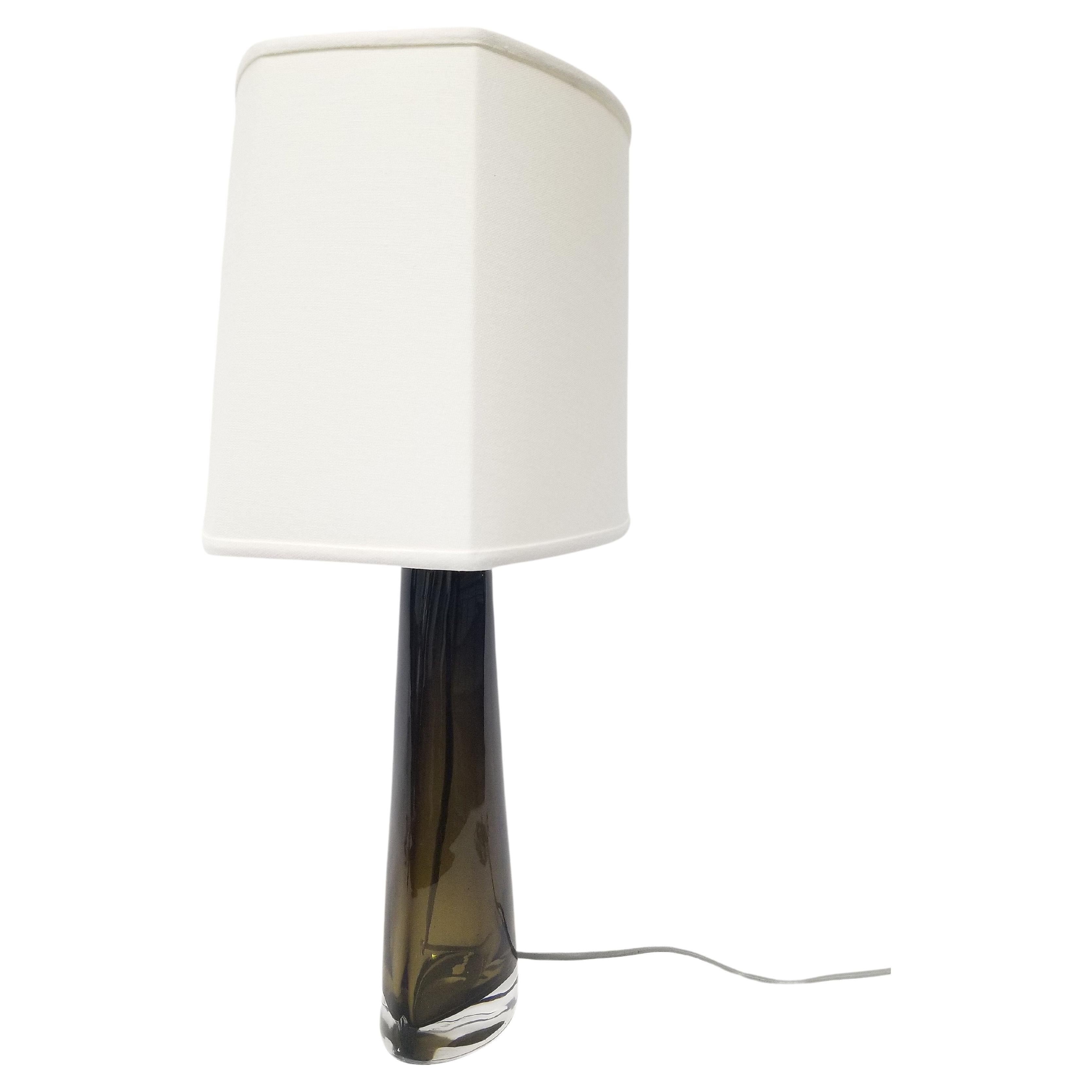 A glass conical table lamp designed by Carl Fagerlund for Orrefors, Sweden, circa 1950s. The lamp features handblown glass in a beautiful smokey olive green hue and a new shade. The custom white shade is uniquely shaped to complement the sleek lines