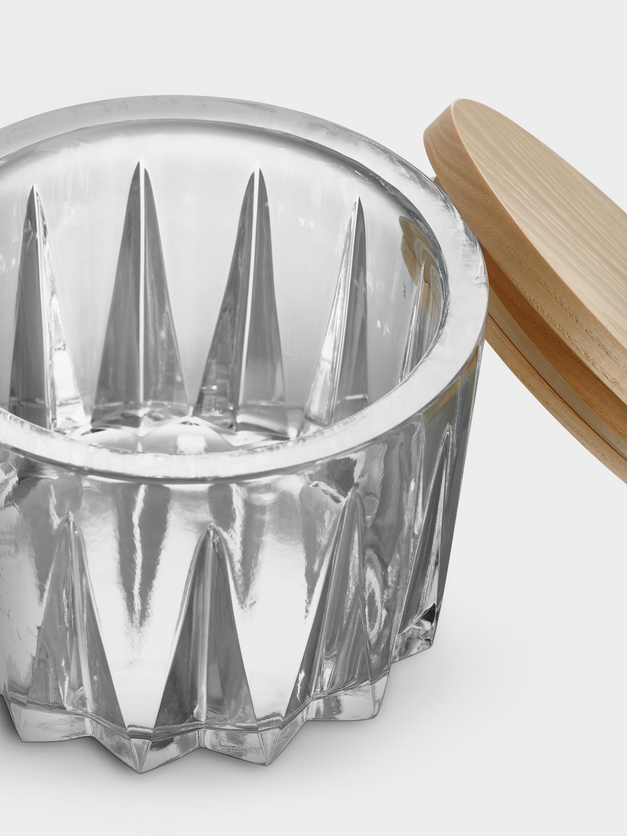 Sarek from Orrefors has deep-cut facets inspired by the motif on wooden baskets made of plaited birch bark, which has a symbolic connection to Swedish nature. The thick crystal bowl has a lid in pale ash wood, providing contrast to the clear glass.
