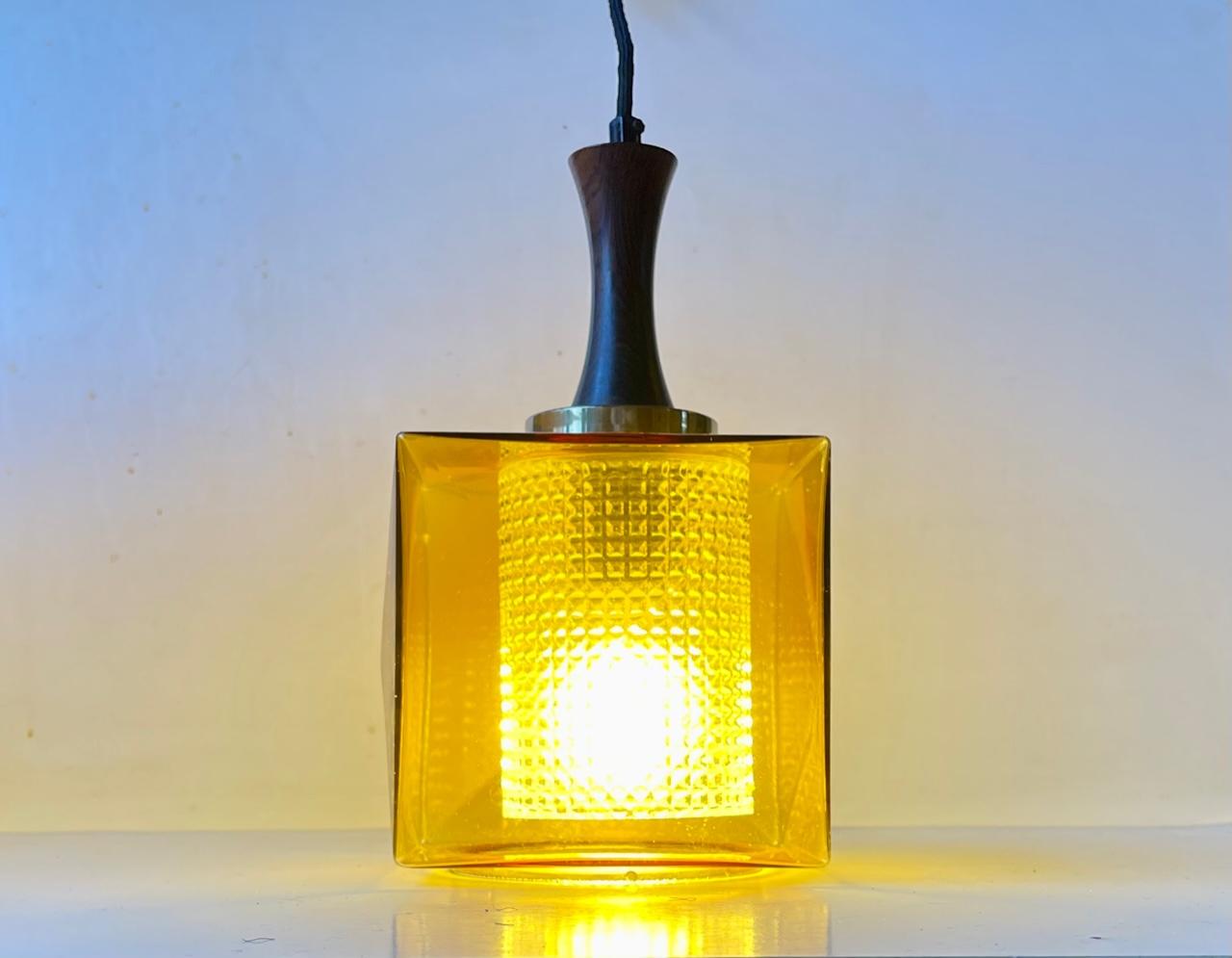 A square hanging light with two glass shades. One exterior in cubic honey glass and one interior in diamond pattern clear glass. Manufactured by Orrefors in Sweden during the 1960s. It features a rosewood top and its original socket. Measurements: