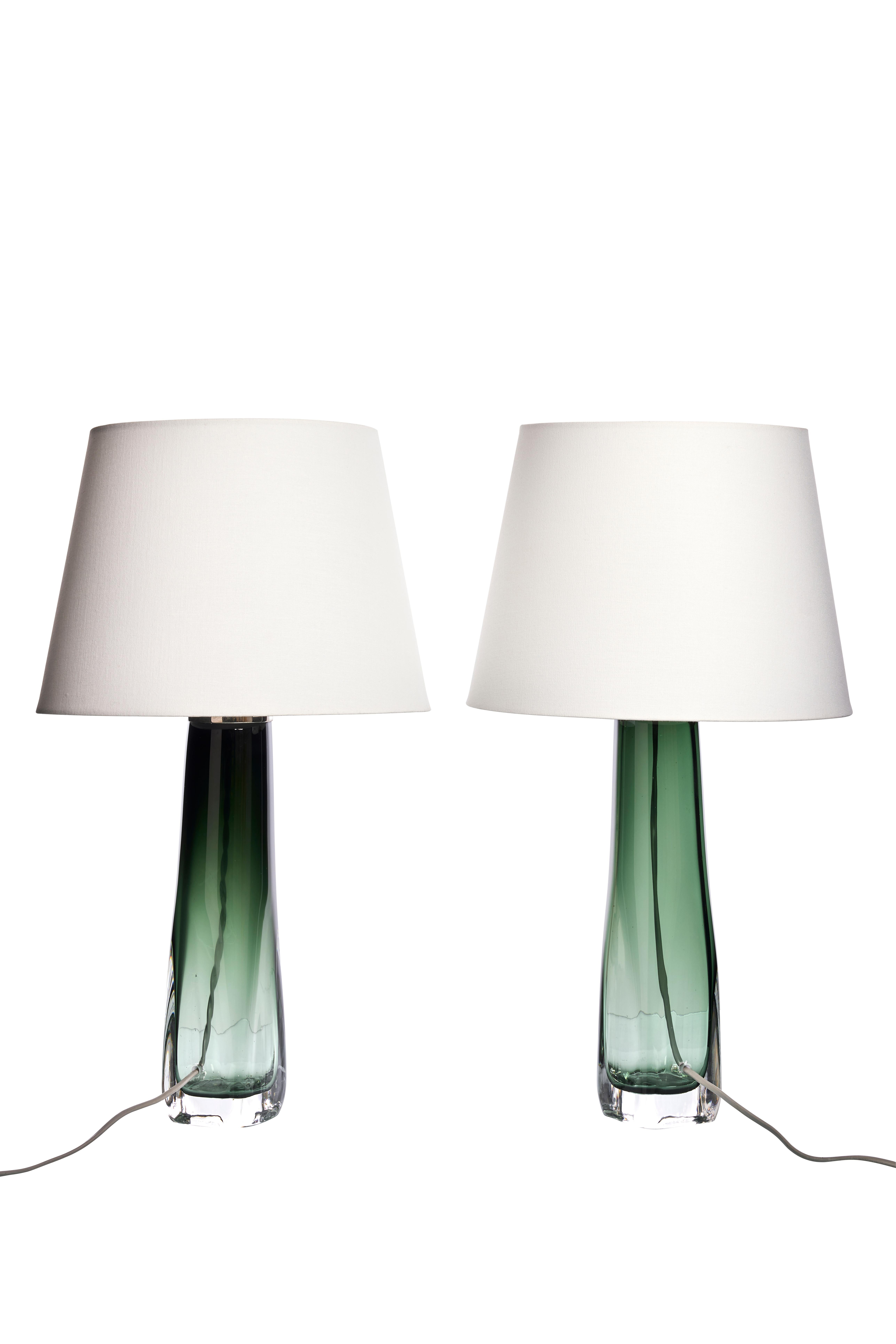 These exquisite table lamps, designed by Carl Fagerlund for Orrefors in the 1960s, embody timeless elegance and sophisticated design. The lamps feature striking green glass bases enveloped in a clear outer layer, creating a captivating visual effect