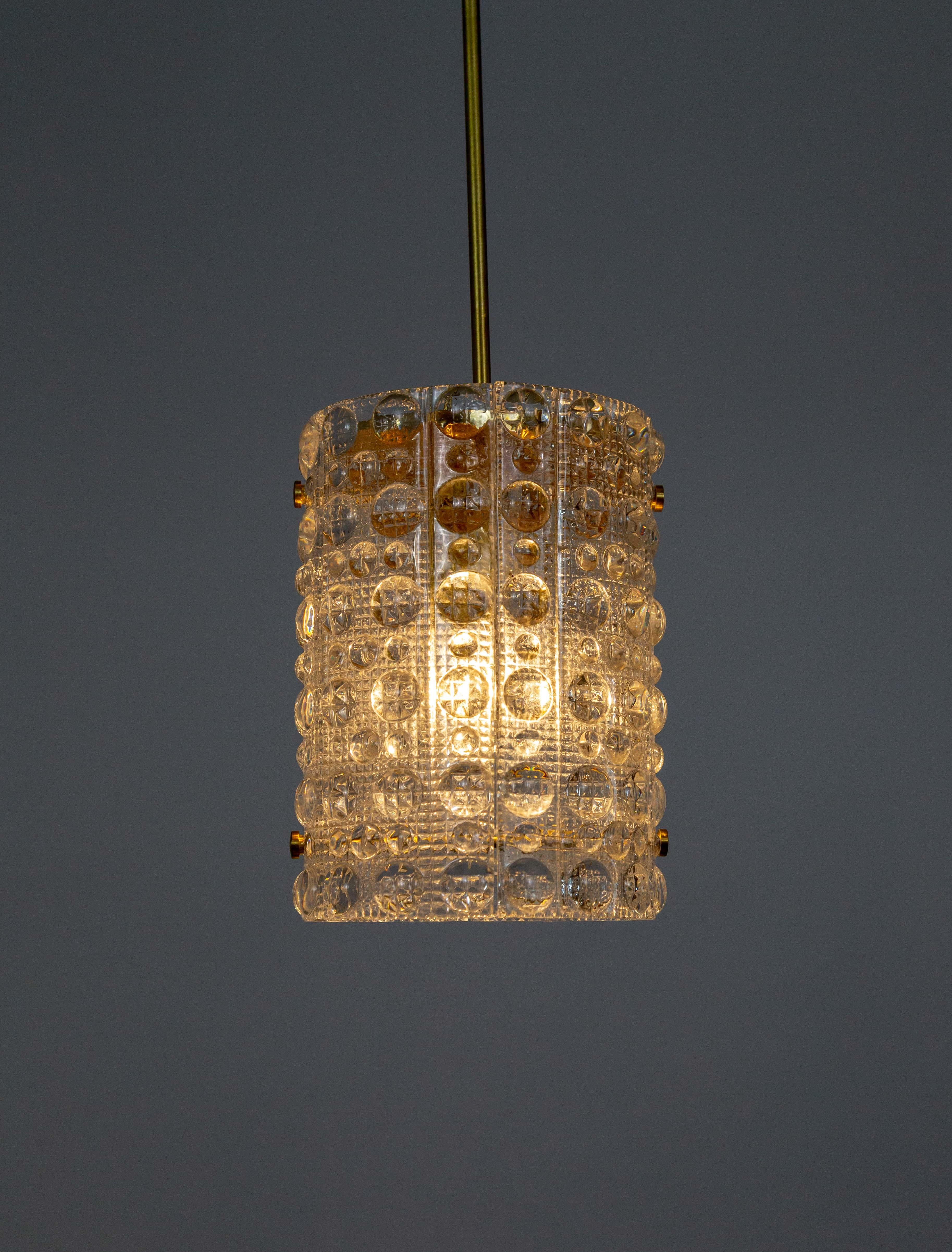 A pendant light from Orrefors by Carl Fagerlund in his Venus-style, cylindrical shaped, molded crystal glass texture. It has a long, narrow brass stem and a spun raw brass top diffuser. The two glass parts are held in place with two inner bars. All