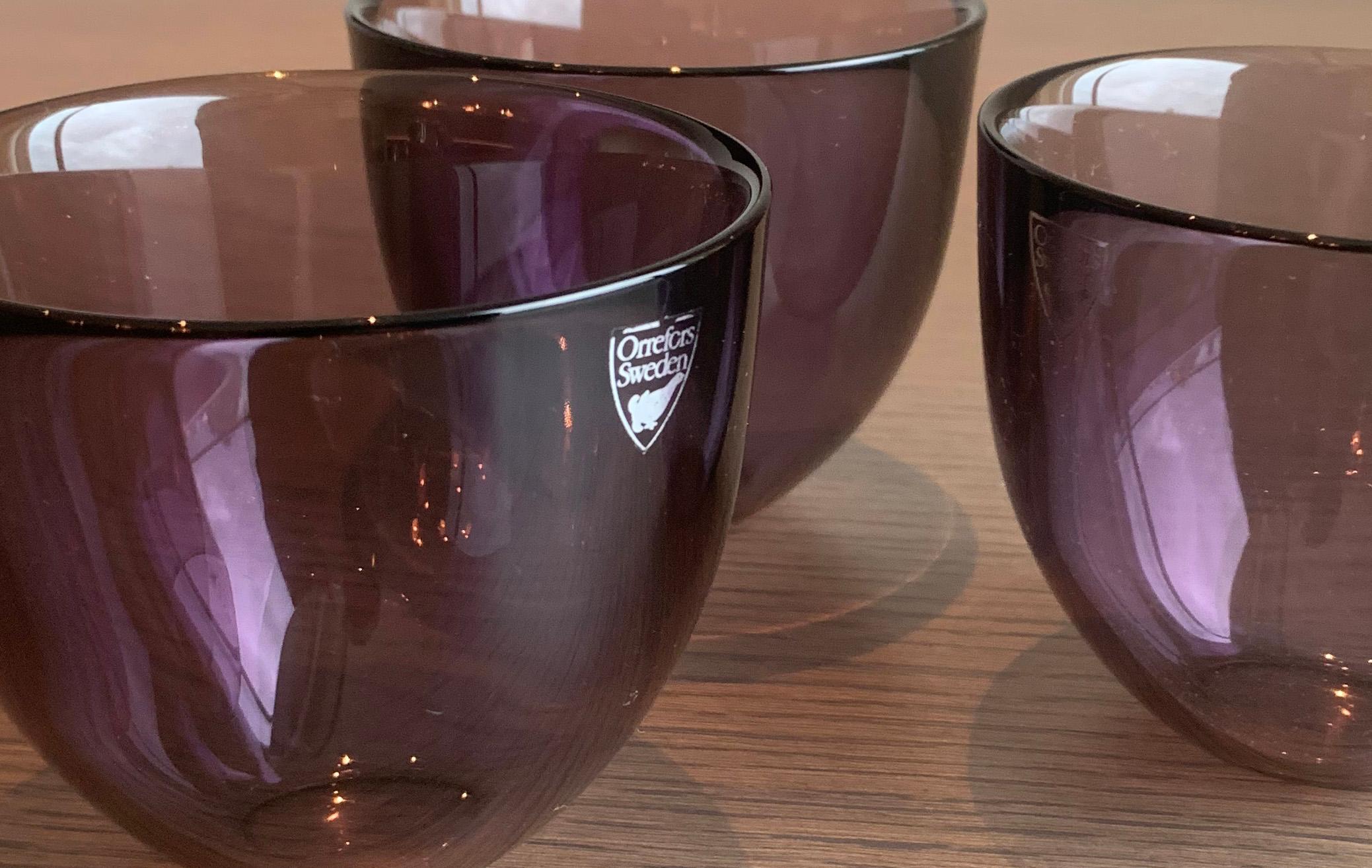 Elevate your home décor with this stunning set of three Amethyst Purple Pastillo Glass Votive Dishes, expertly crafted by renowned designer Lena Bergstrom in collaboration with famed Swedish crystal makers Orrefors.

Featuring a unique and modern