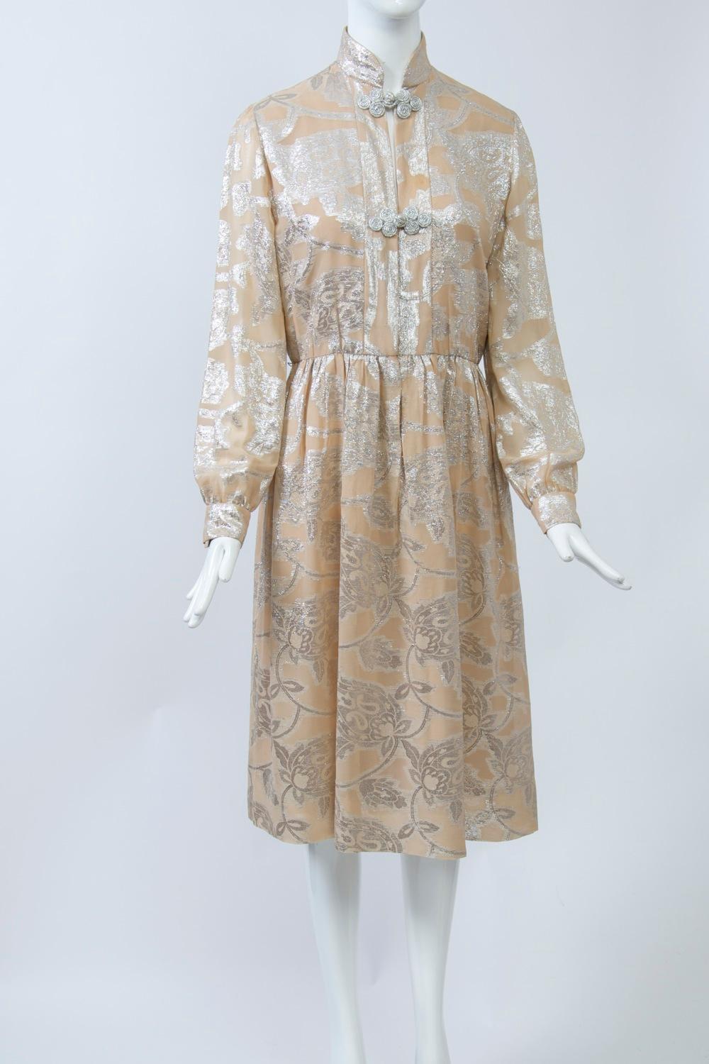 Oscar de la Renta dress c.1970 crafted of a sheer beige fabric shot through with silver metallic thread in a large abstract floral pattern. Modified shirtwaist style with front opening that featrues 2 silver thread frog closures, one at the mandarin