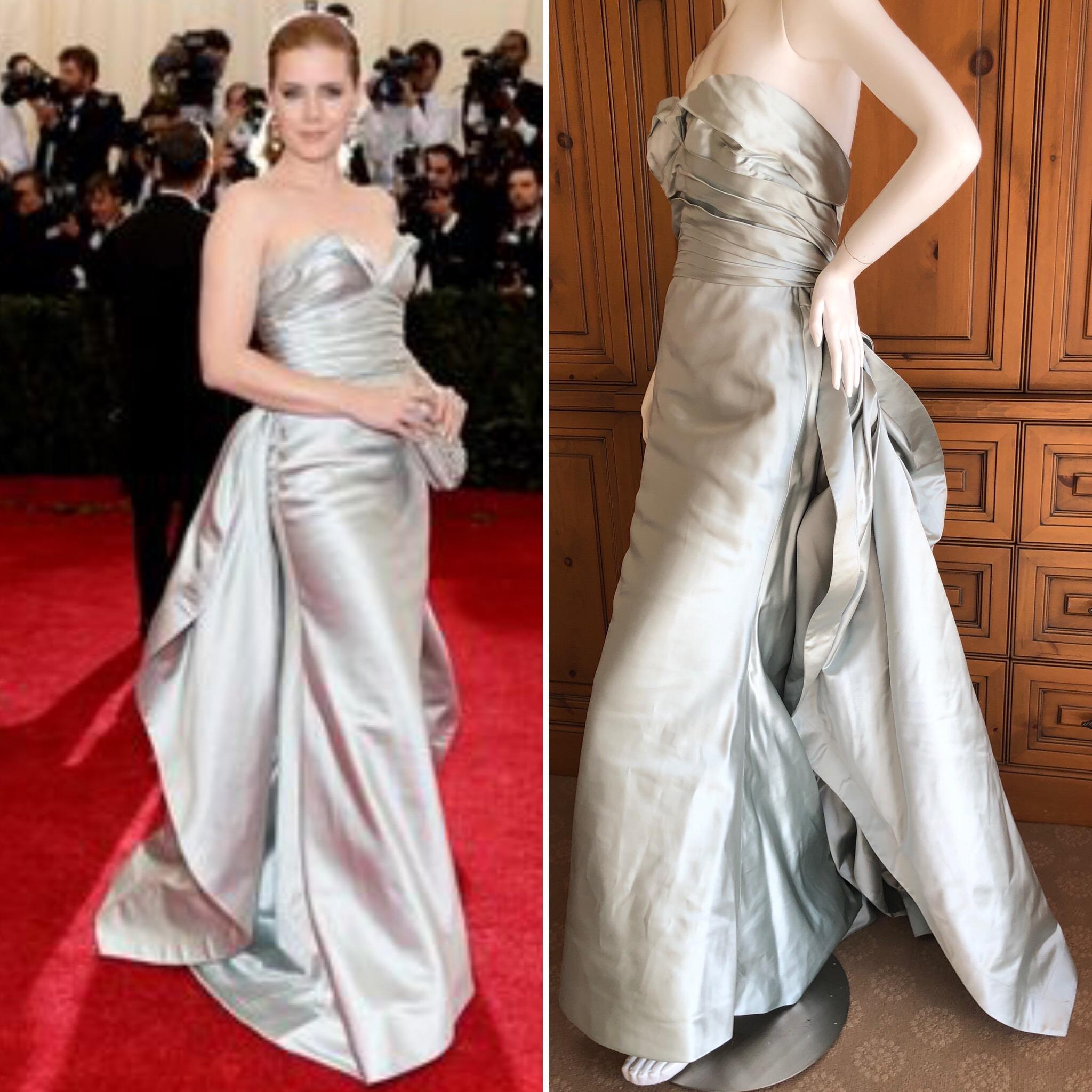 Oscar de la Renta Spectacular 2014 Met Ball Silver Strapless Ballgown.
Worn by Amy Adams to the Met Ball, this is an homage to Charles James , with two winglike trailing train's.
There is an inner bustier.
Simply Stunning. Please use the zoom