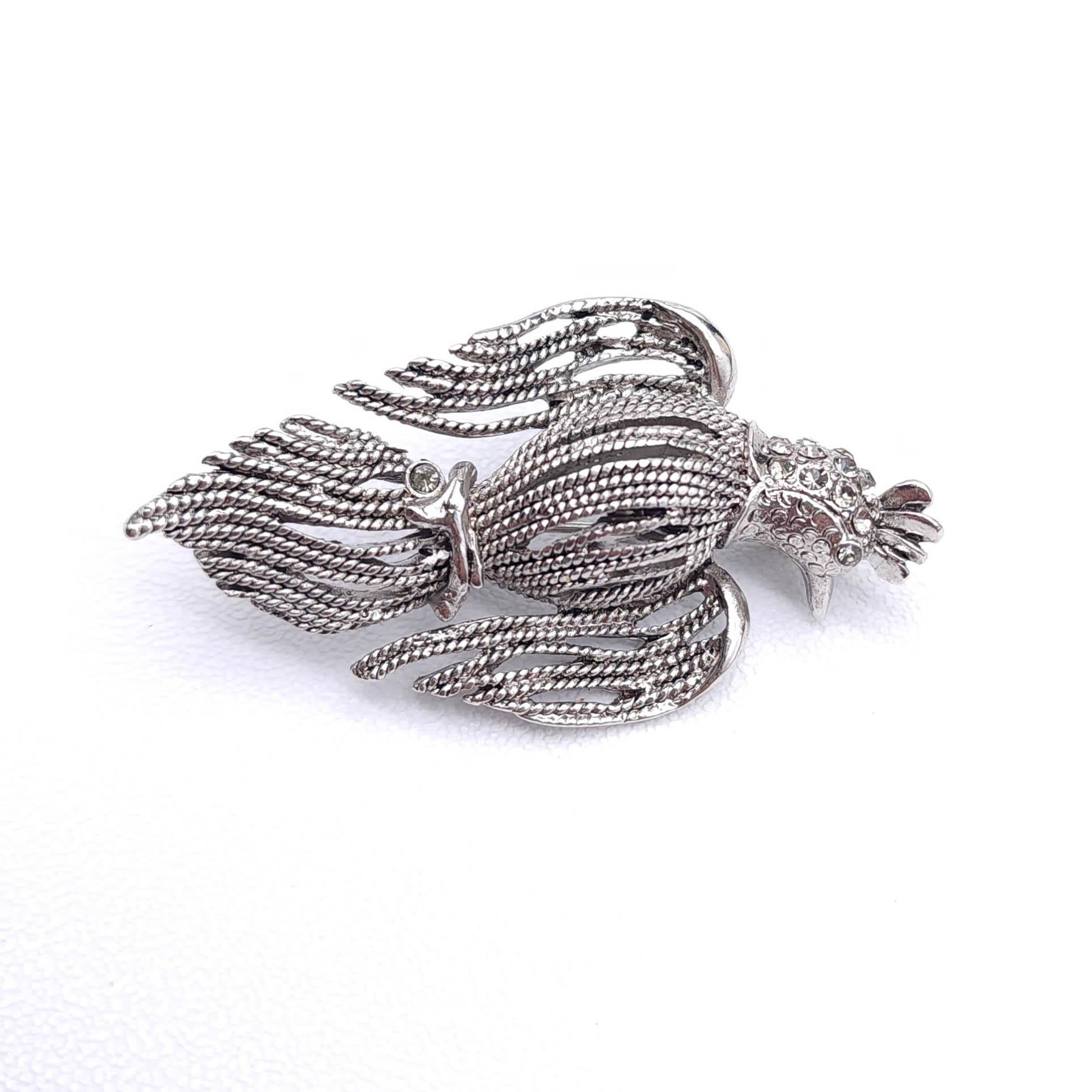 Schmücken Sie Ihr Ensemble mit der bezaubernden Vogel-Brosche von Oscar de la Renta, einem Meisterwerk an Design und Handwerkskunst! Dieses exquisite Stück ist mit einer strukturierten silberfarbenen Oberfläche versehen, die ihm einen raffinierten