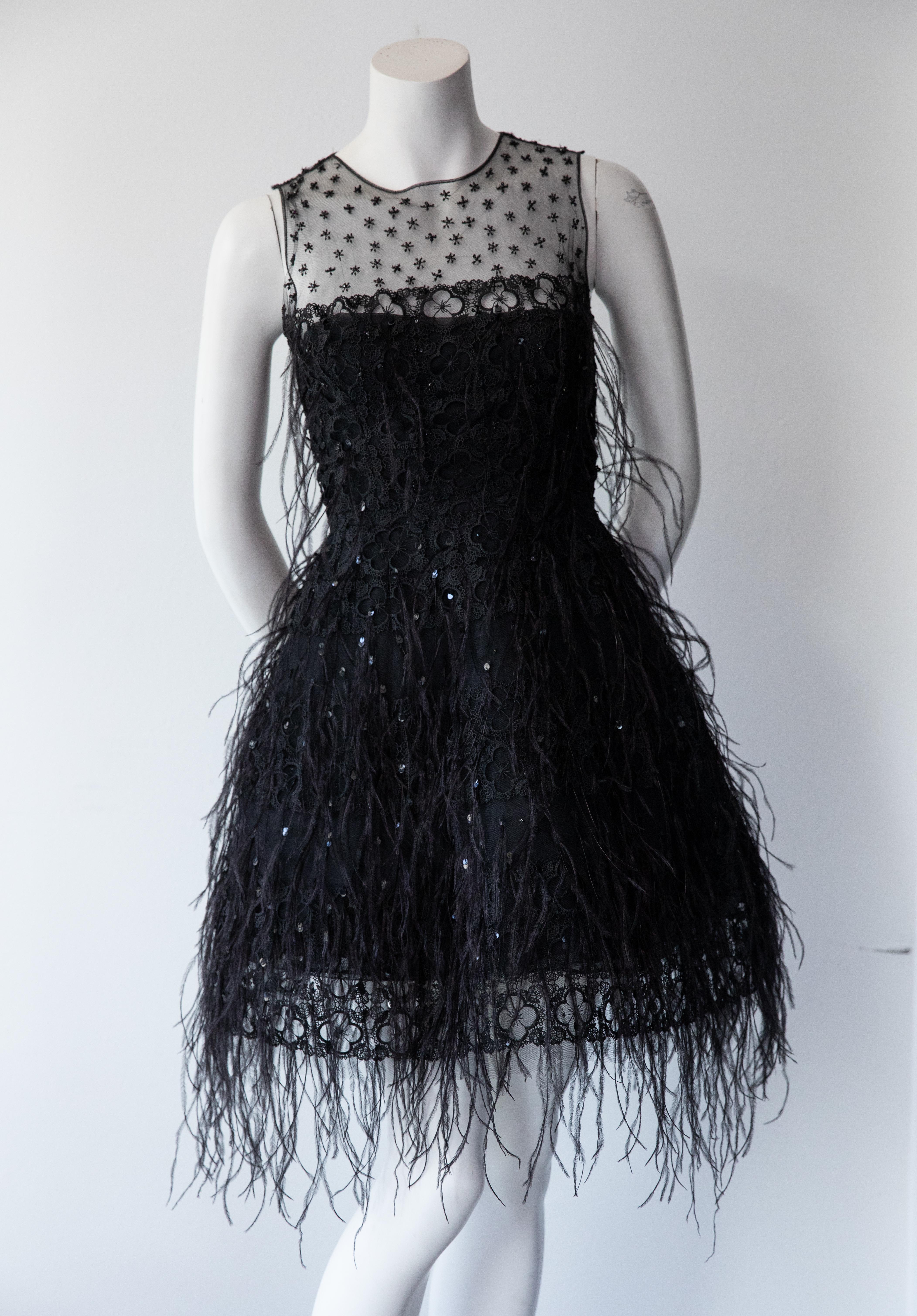 In this structured Oscar De La Renta cocktail dress you will embody the essence of classic, elevated glamour. Black feathers and rhinestones add texture to this sleeveless black dress, while the embroidered sheer mesh yoke adds reveals the slightest