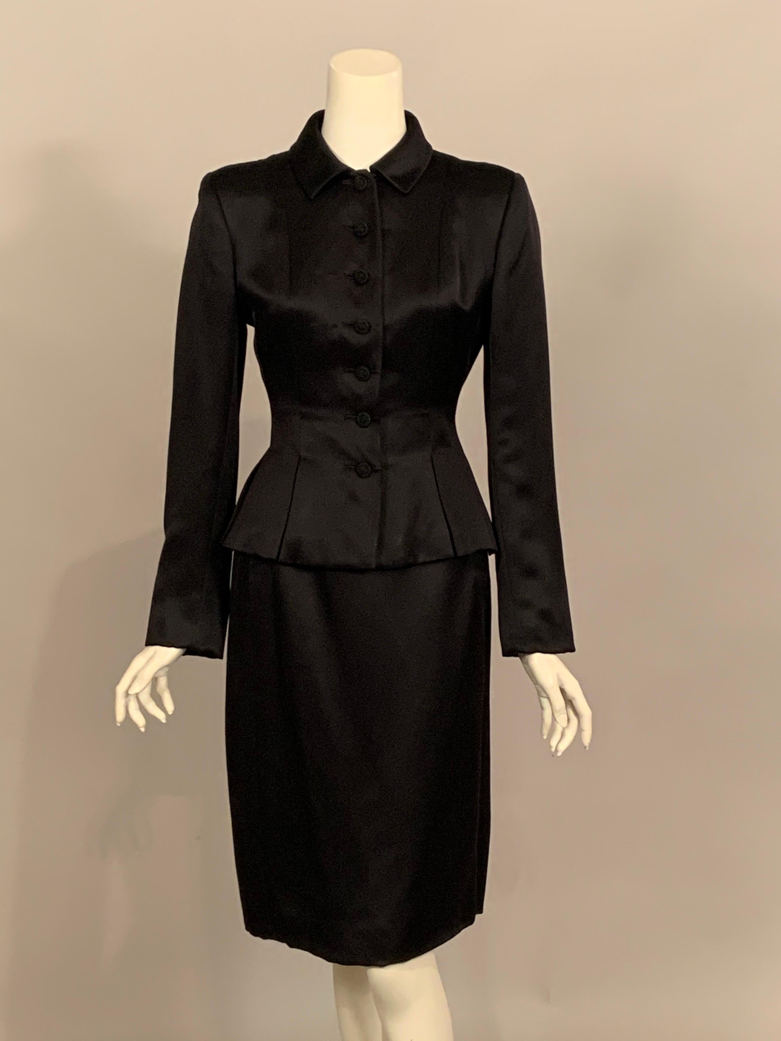 Timeless elegance is the best way to describe this black silk satin suit designed by Oscar de la Renta.  The jacket has a small round collar and seven passementerie buttons at the center front.  The peplum has nine inverted pleats reminiscent of the