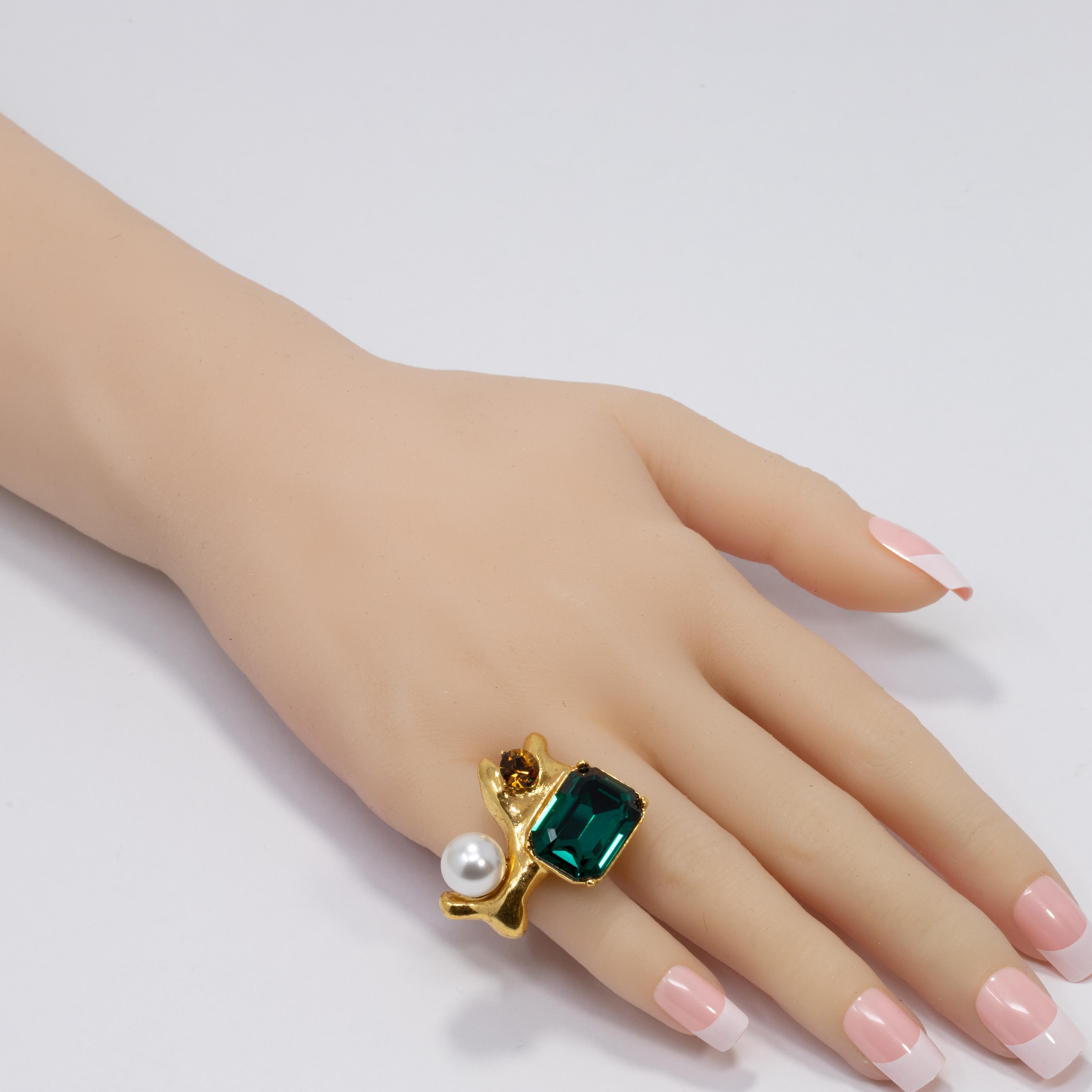 A bold statement ring by Oscar de la Renta. Features two prong set crystals, one in emerald green and the other in amber-orange, accented with a single faux pearl. Set on a stylized gold plated band.

Ring size: Adjustable, US 4-8
Face dimensions: 3