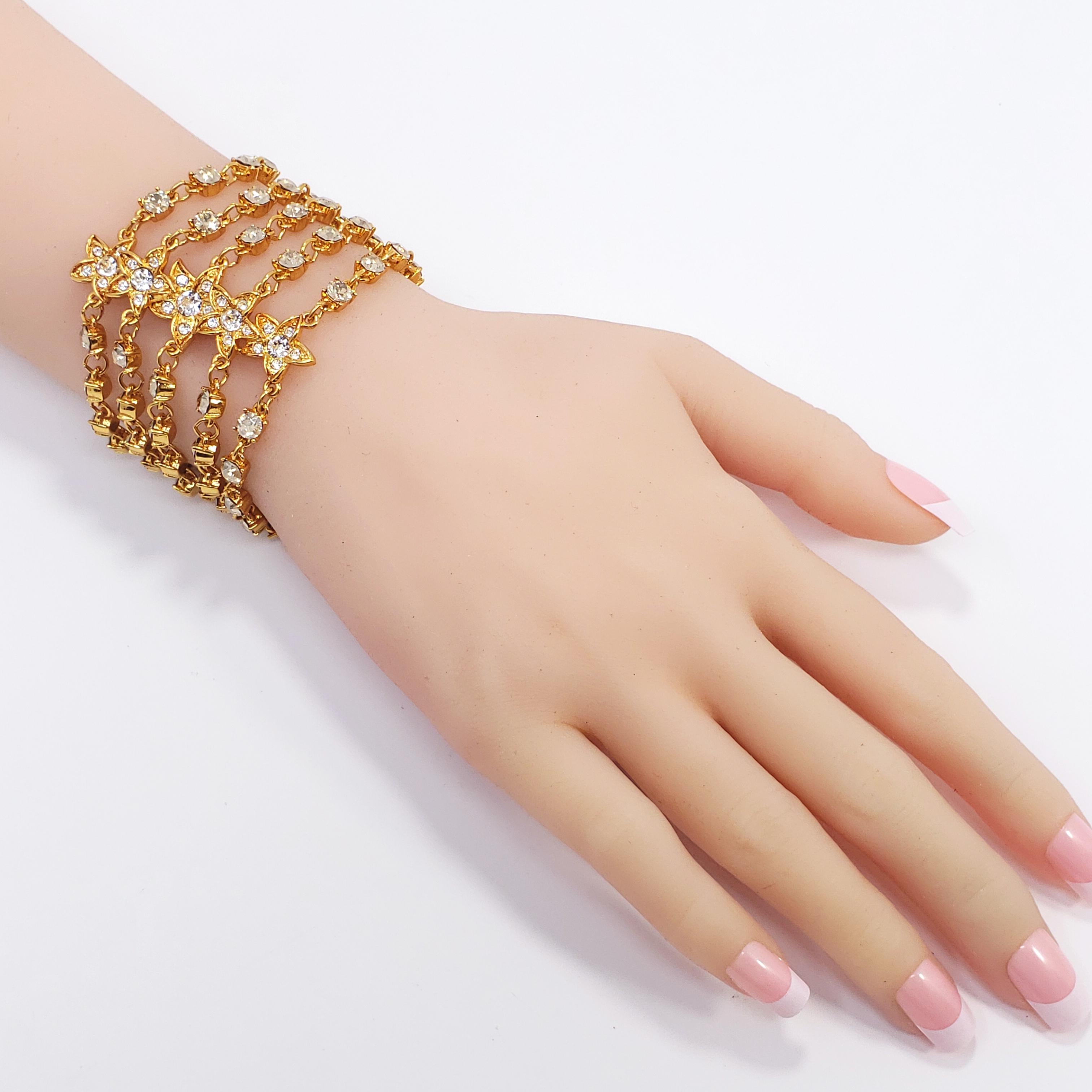Dieses Armband von Oscar de la Renta besteht aus fünf Strängen mit goldfarbenen Kettengliedern, die mit Kristallen in Zackenfassung und floralen Motiven verziert sind. Ein Funkeln wie kein anderes!

Verschluss mit Knebelschließe.
Markenzeichen: