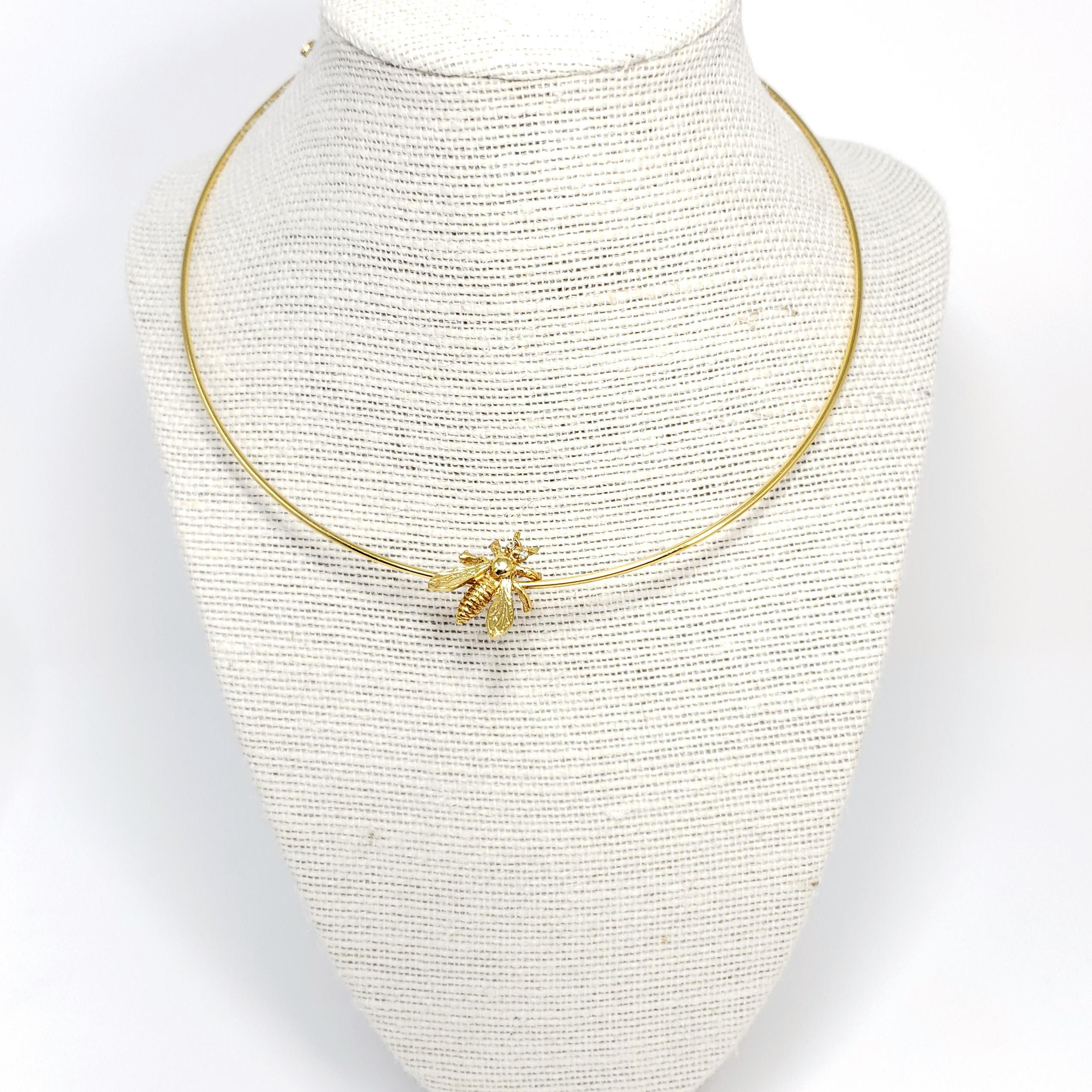 A golden wire choker accented with a bee, by Oscar de la Renta.

Gold-plated.

Hallmarks: Oscar de la Renta, Made in USA
