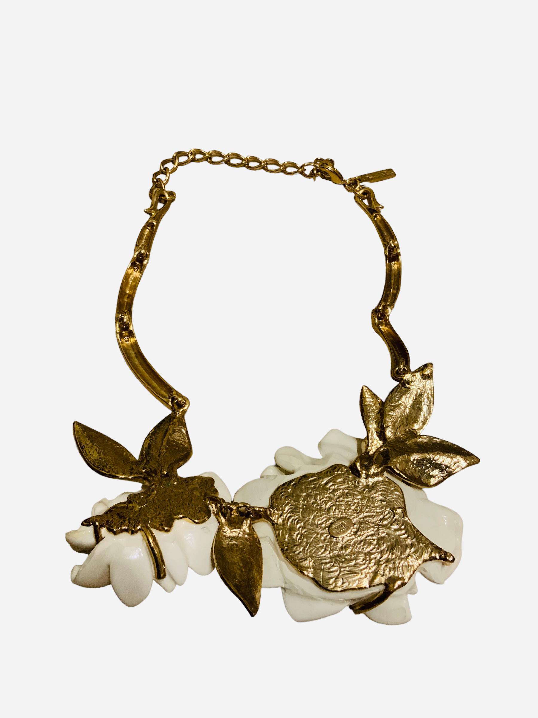 This is an Oscar de la Renta gold plated choker-chain necklace. It has long gold plated bar links that end with a bouquet of two ivory color resin Camellias flowers with leaves adorned with rhinestones. It has a gold plated tag hallmarked Oscar de