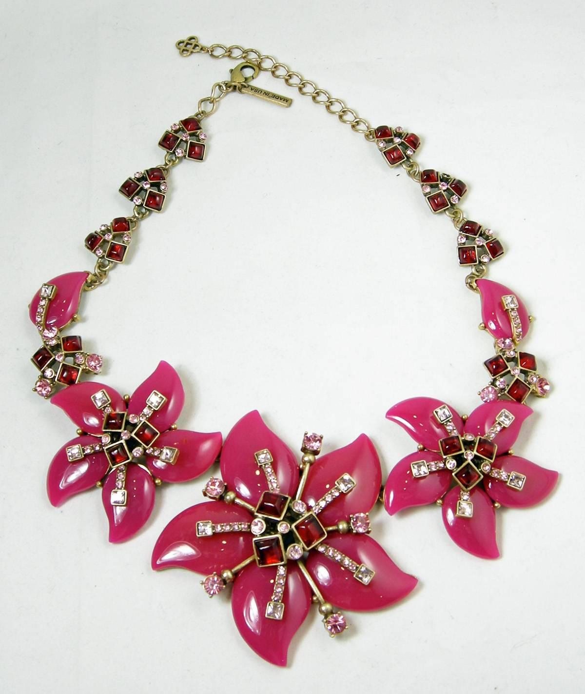This signed Oscar de la Renta necklace features a floral design with hot pink enamel flowers that have pink and clear crystal petals in the middle of the flowers. The centers of each flower are red cabochons bezel set in a gold tone setting.  Red